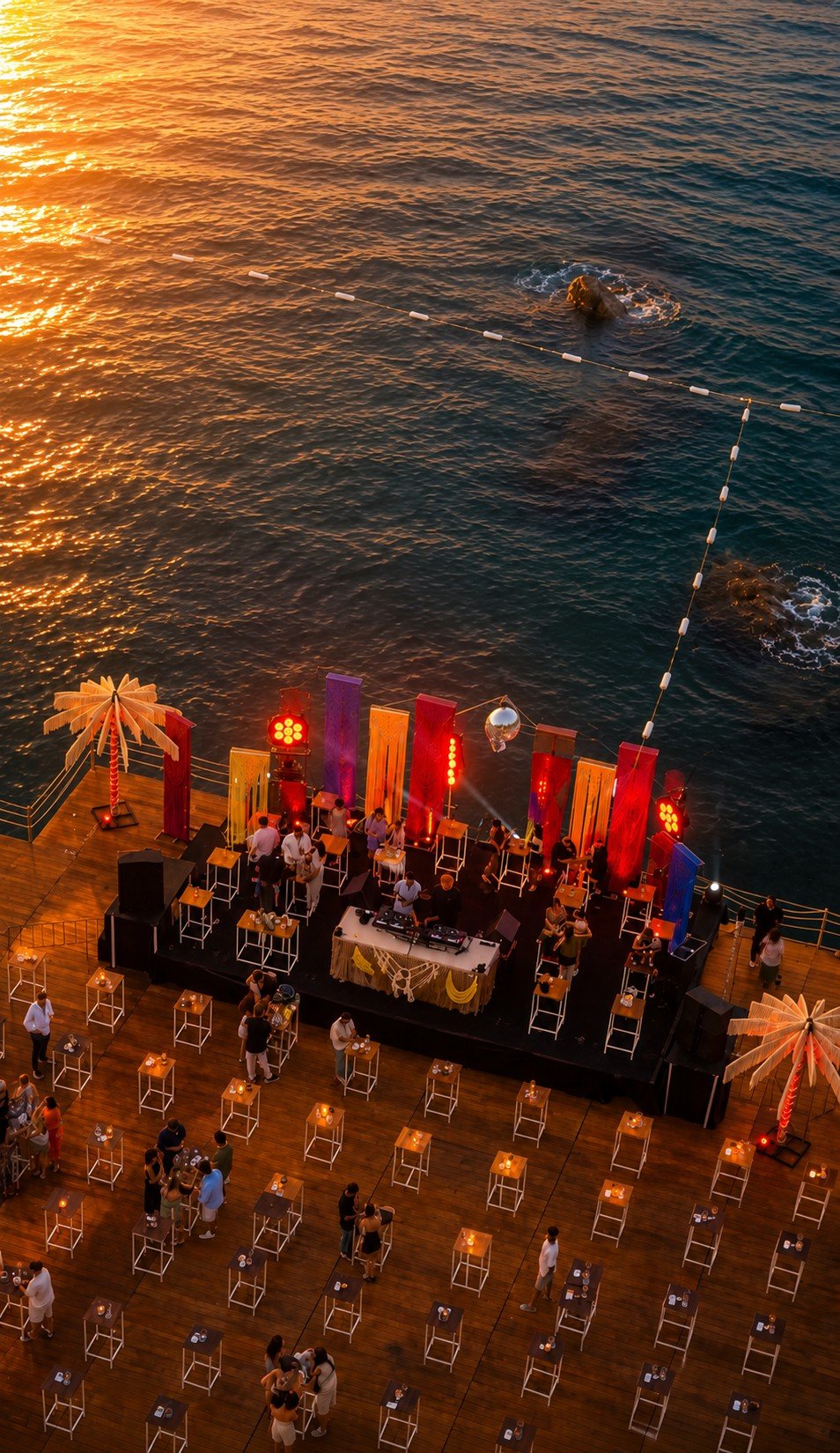The Dimare-dressed Bilem Beach stage seen from above, crimson fibre-art columns against the sea at sunset