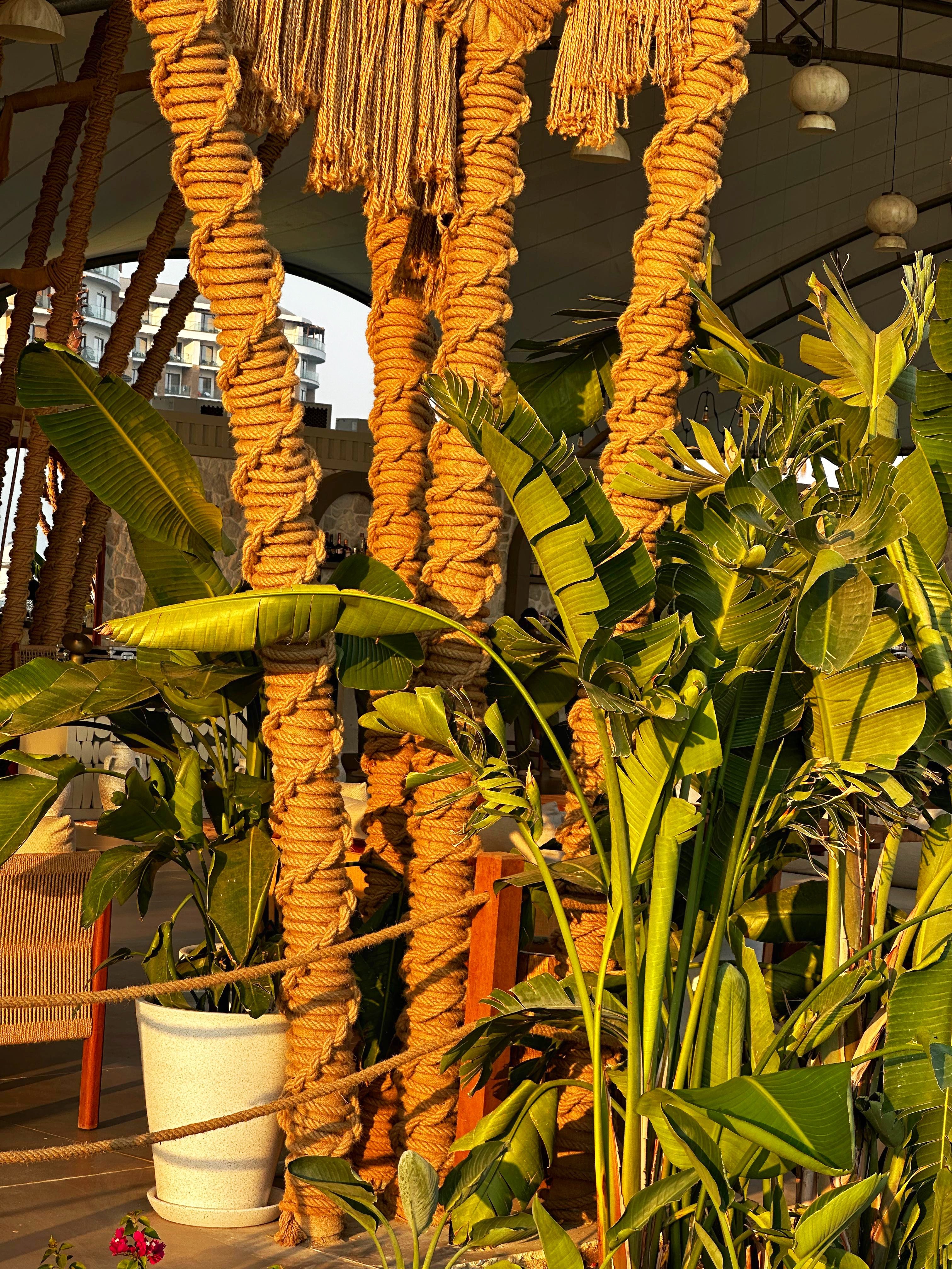 Detail of Dimare hand-twisted macramé rope columns in warm ochre tone amid greenery at Ethno Hotels Belek