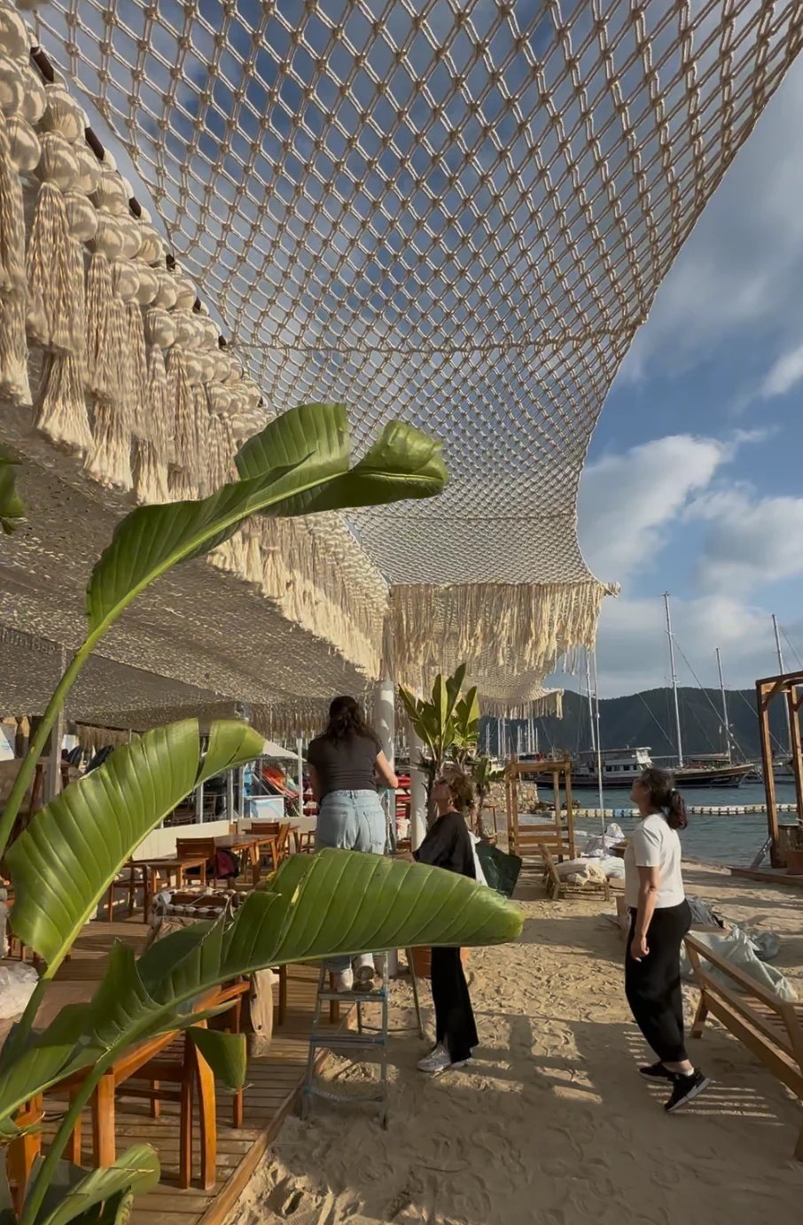 A cream knotted canopy and fringe above an outdoor seating area, with people working below.