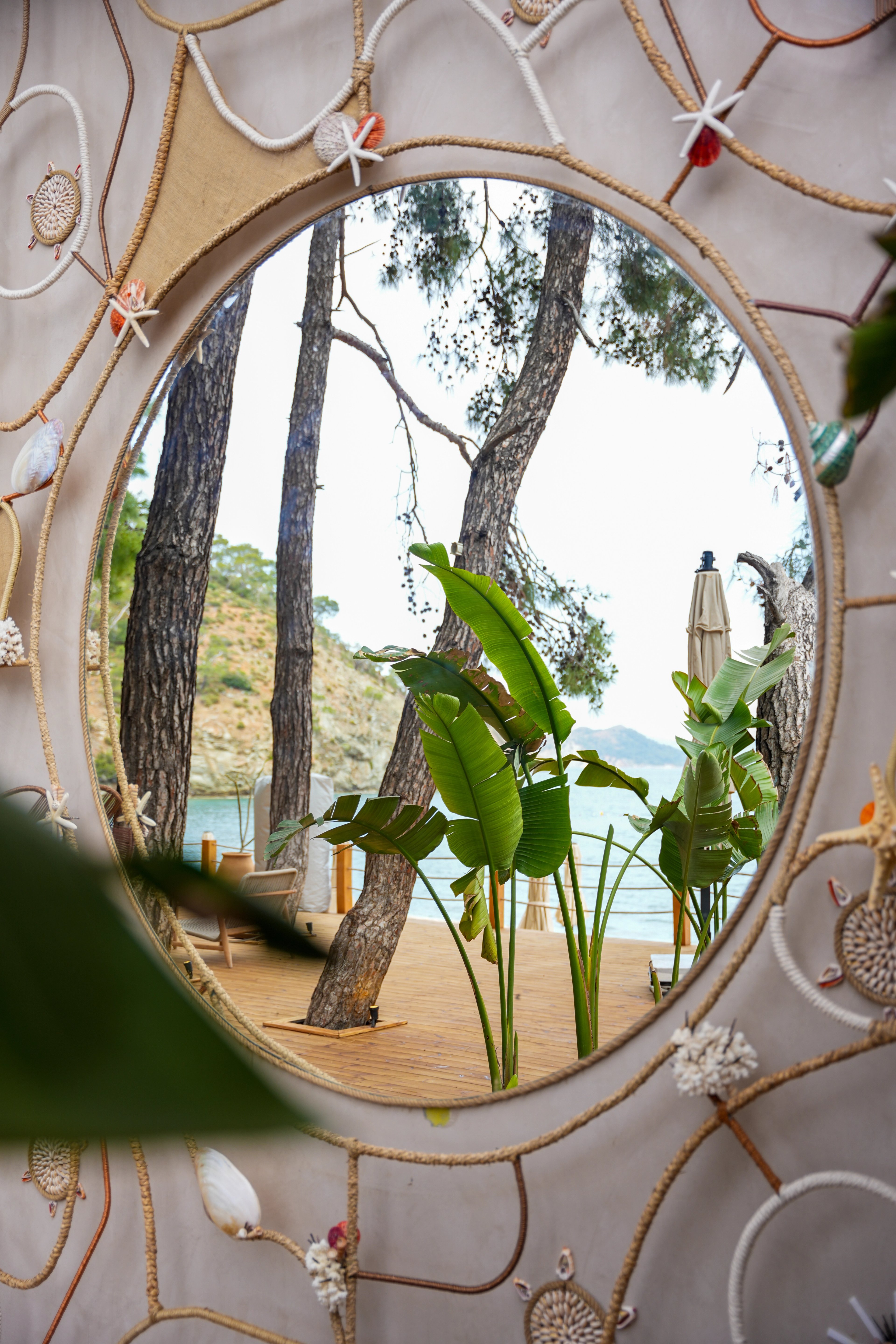 Close view of a round mirror reflecting trees and the beach beside decorative rope lines at So Beach.