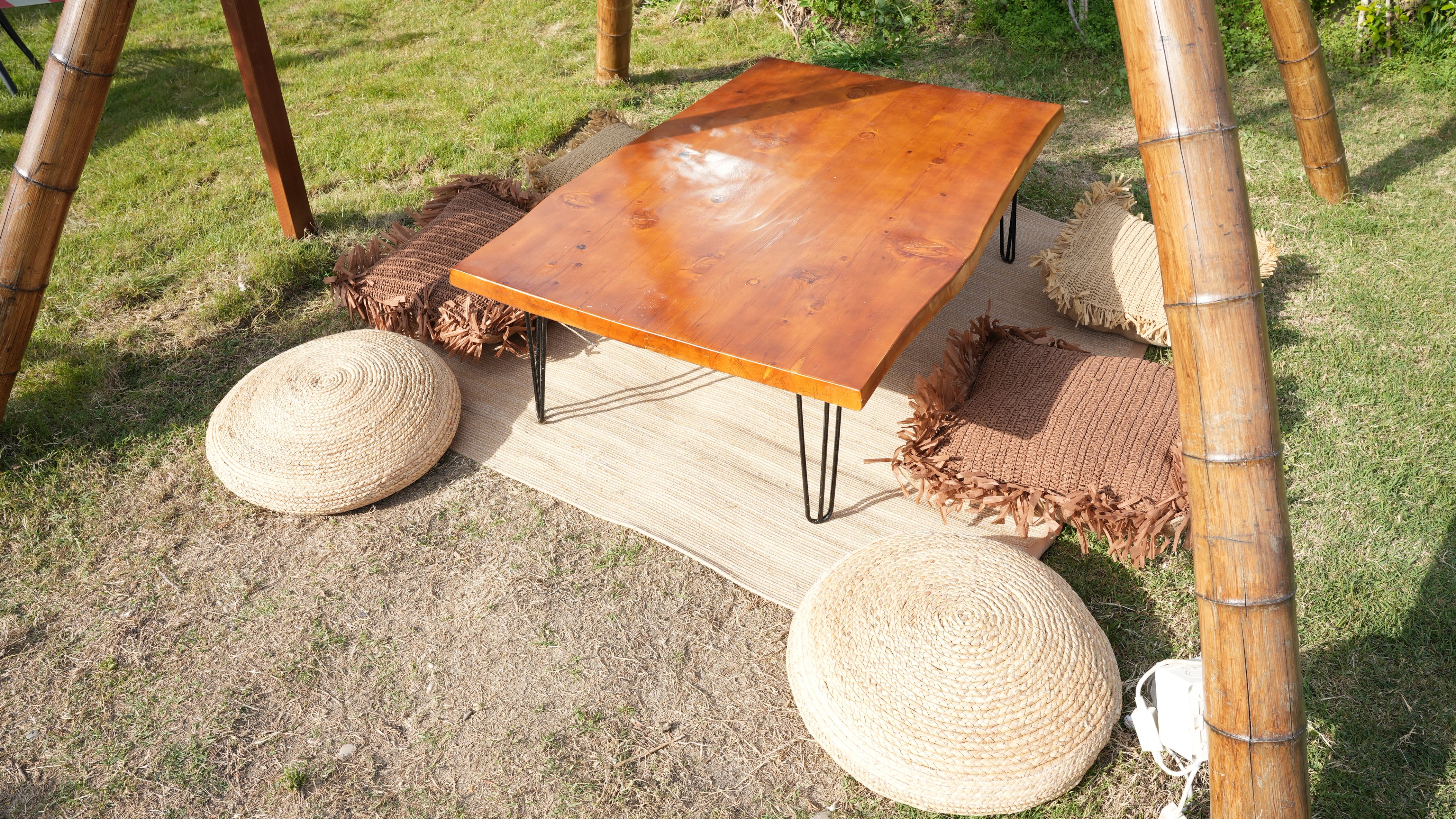 Round woven poufs and fringed floor cushions around a low rectangular timber table in the garden at Lucky Monkey Hotel.