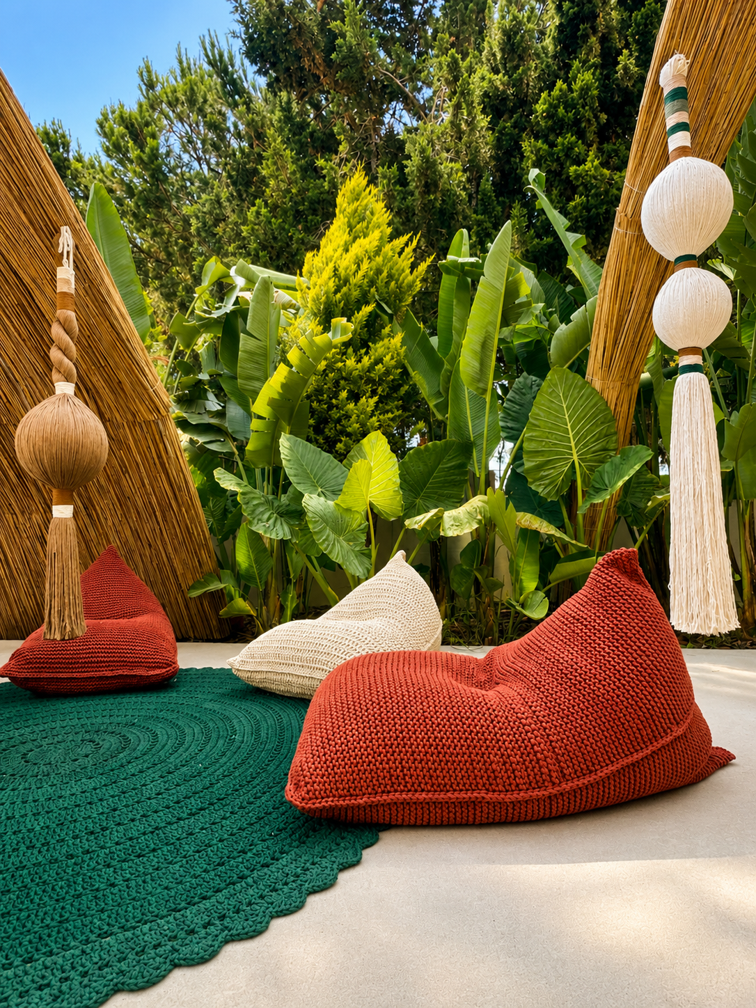 Terracotta and cream woven floor cushions beside a green round rug and hanging tassels among planting at Adalya Bliss.