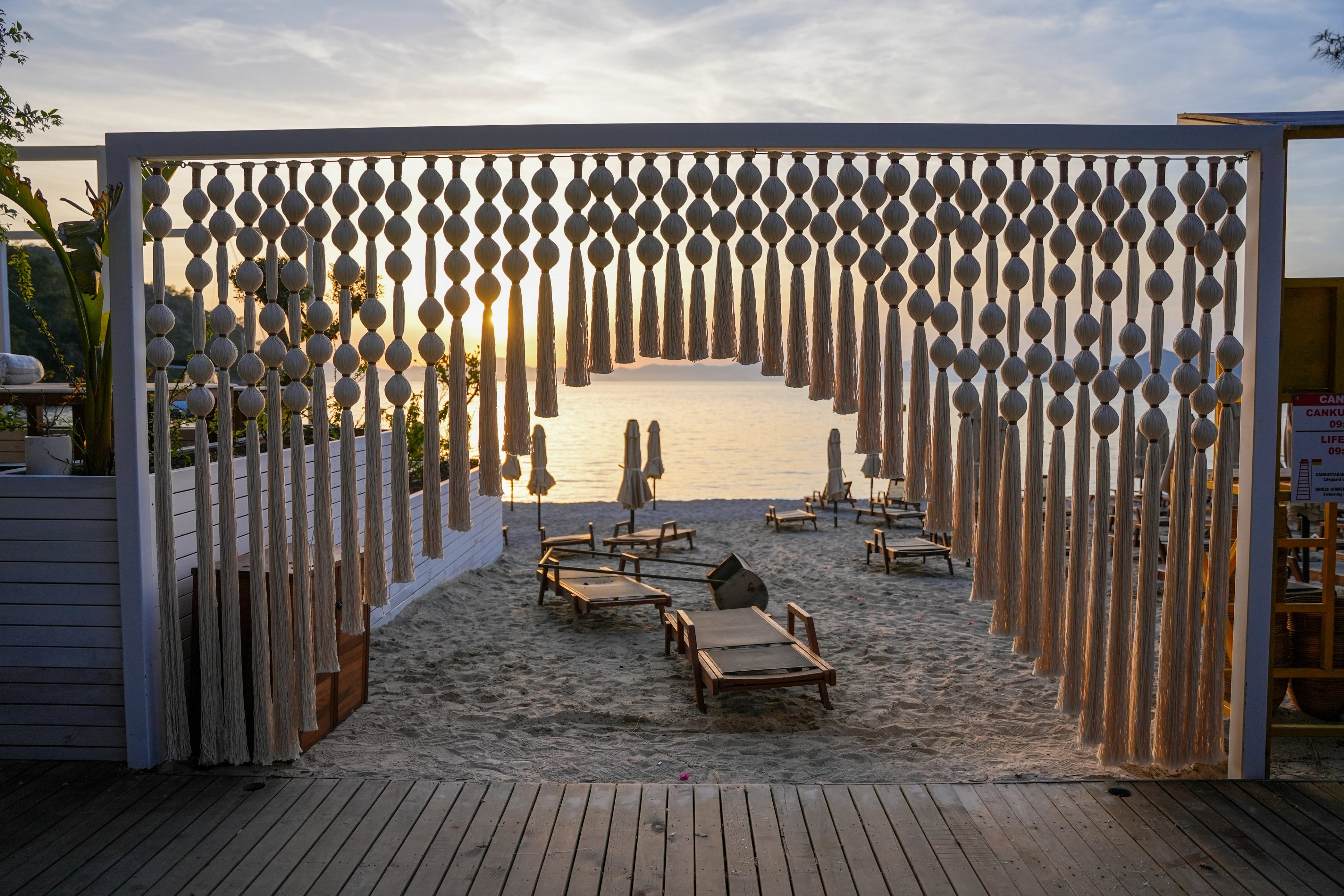 A cream sphere-and-tassel screen forming an arched opening toward beach loungers and the sunset at So Beach.