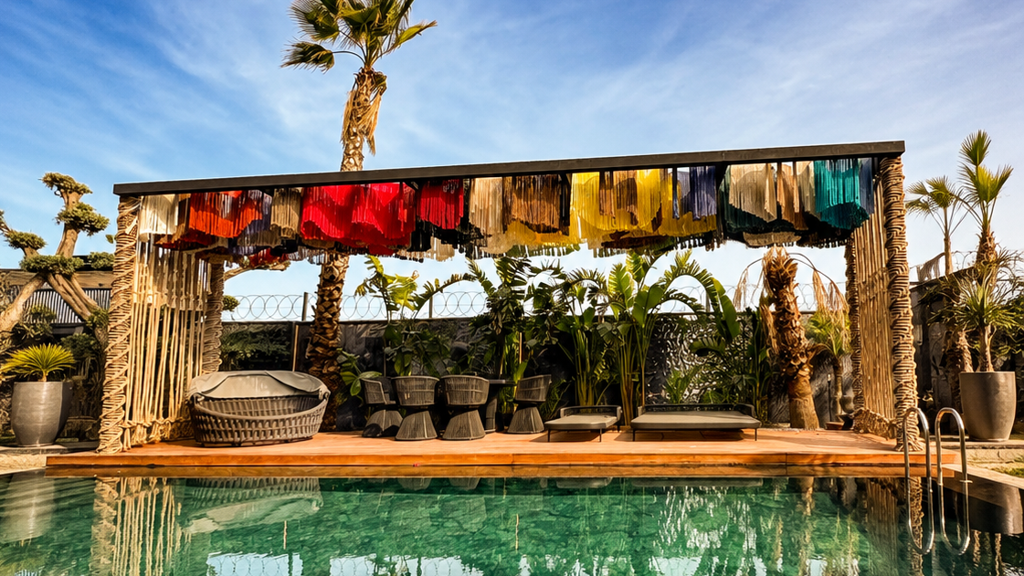 A poolside pergola with multicoloured fringe panels and rope-wrapped posts reflected in the water at a private residence.