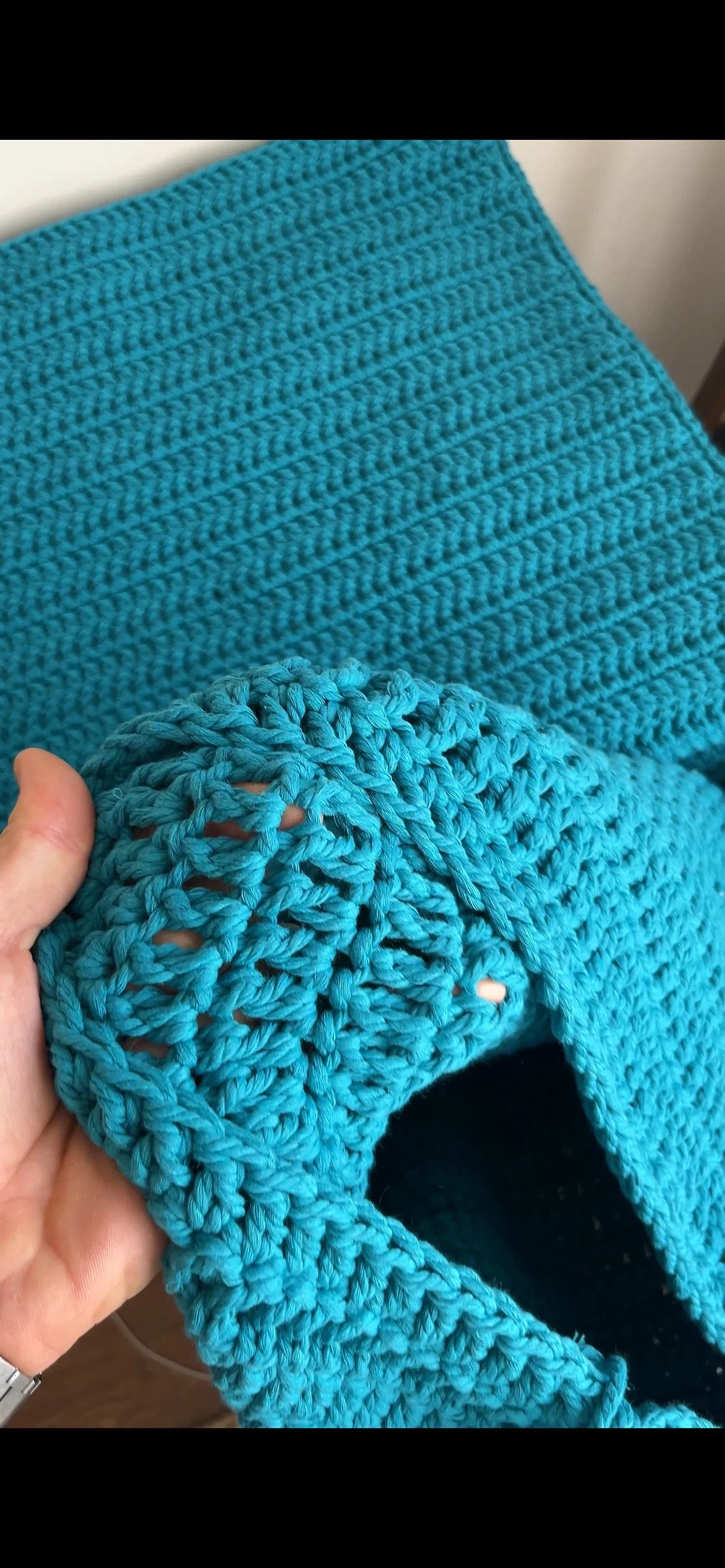 A hand holding the edge of a turquoise crocheted textile.