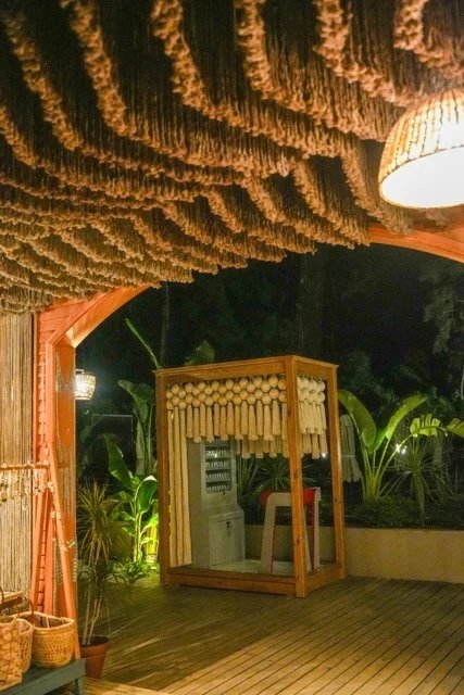 A dark fringed ceiling and pendant light above a timber deck, with a cream decorative panel beyond at So Beach.