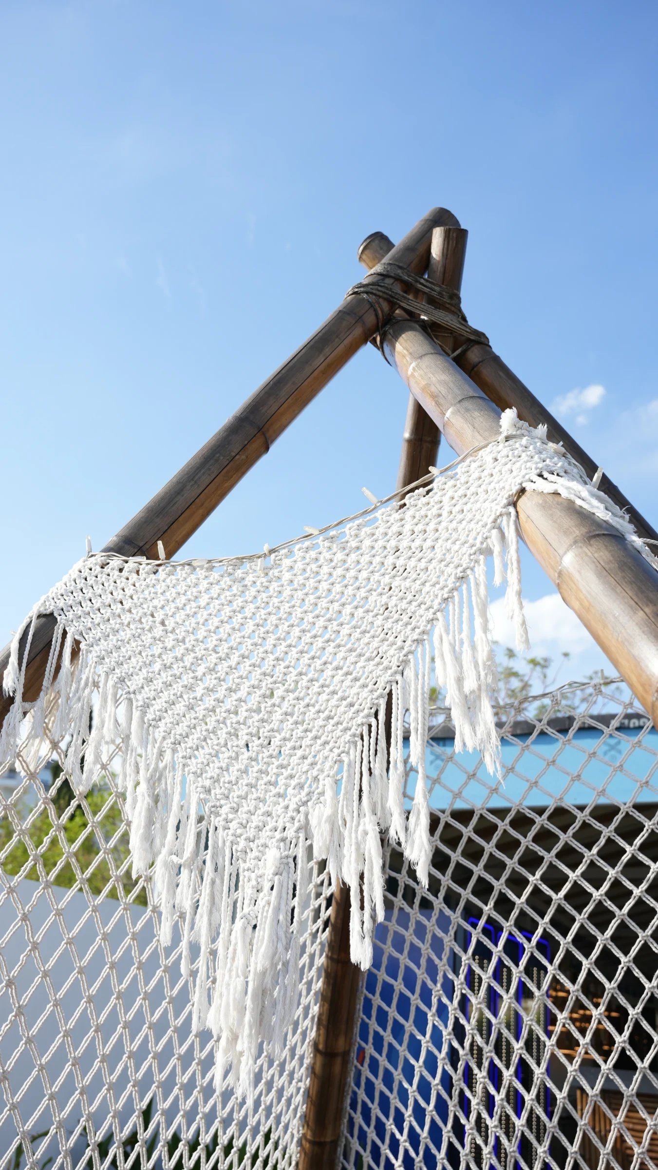 Detail of a Dimare macramé panel with long fringe hung from the bamboo frame against the sky