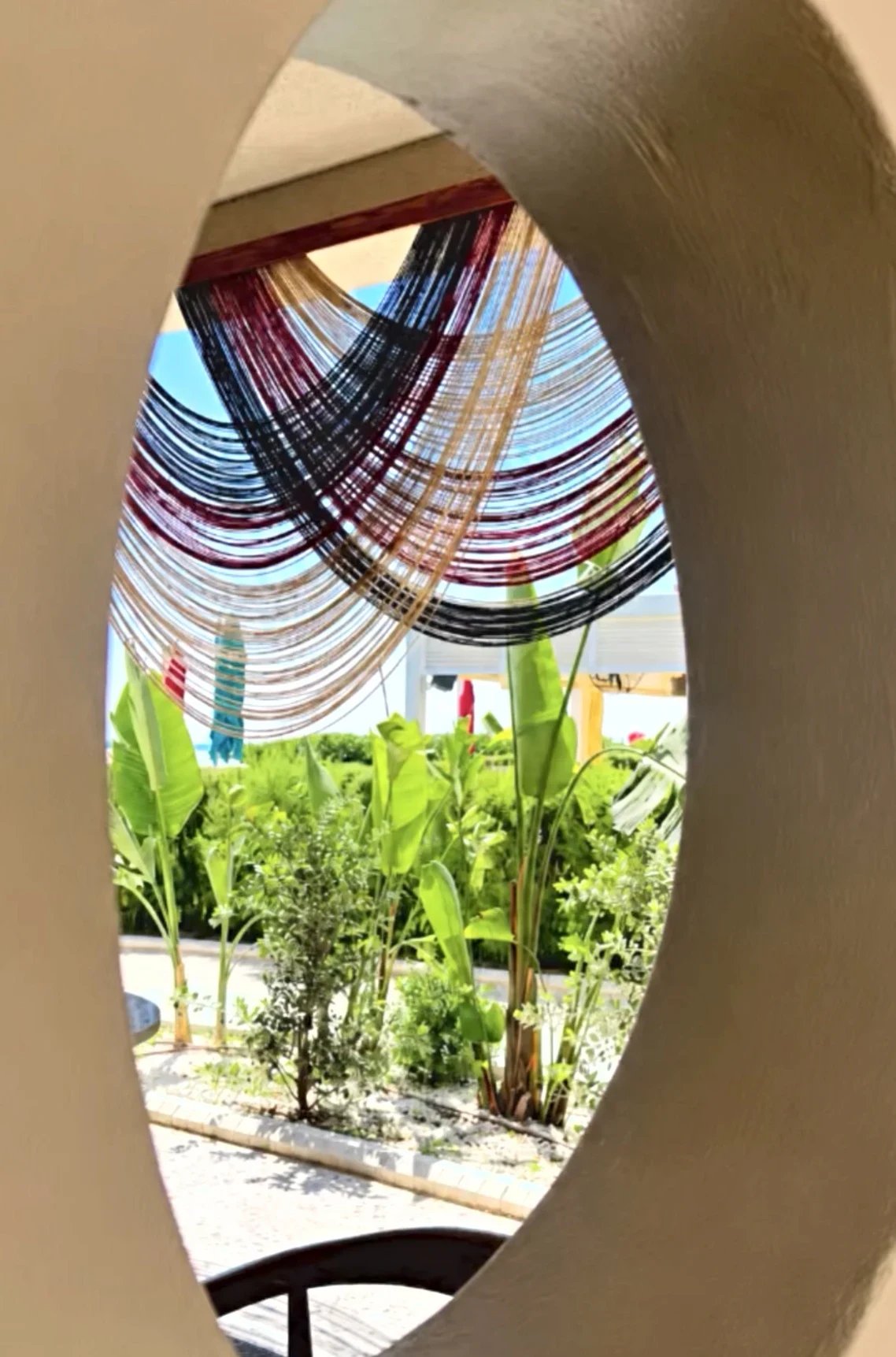A multicolour thread canopy strung above the Adalya Bliss garden, seen through an oval opening in the wall