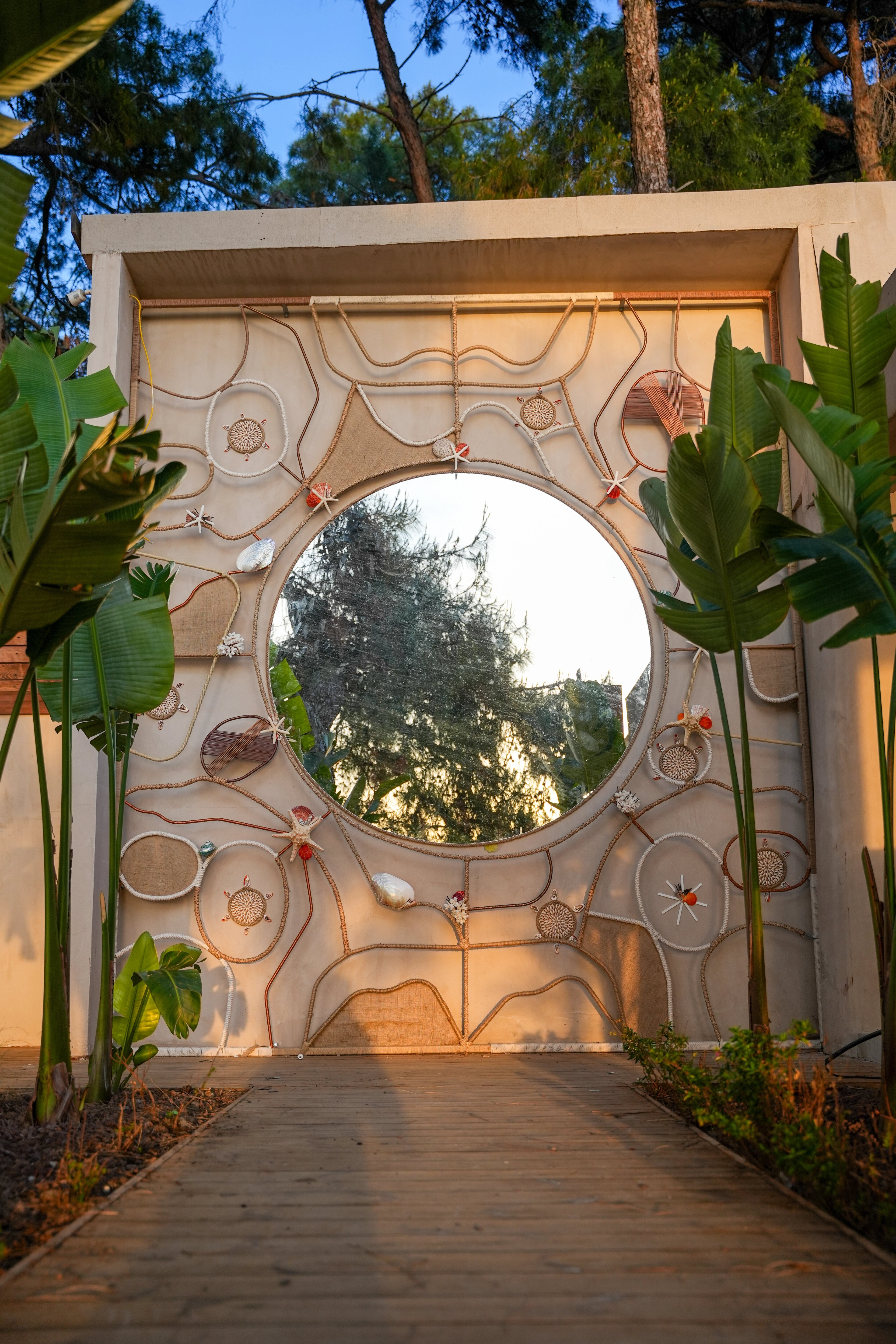 A large round mirror within a wall composition of curved rope lines, shells and circular details at So Beach.