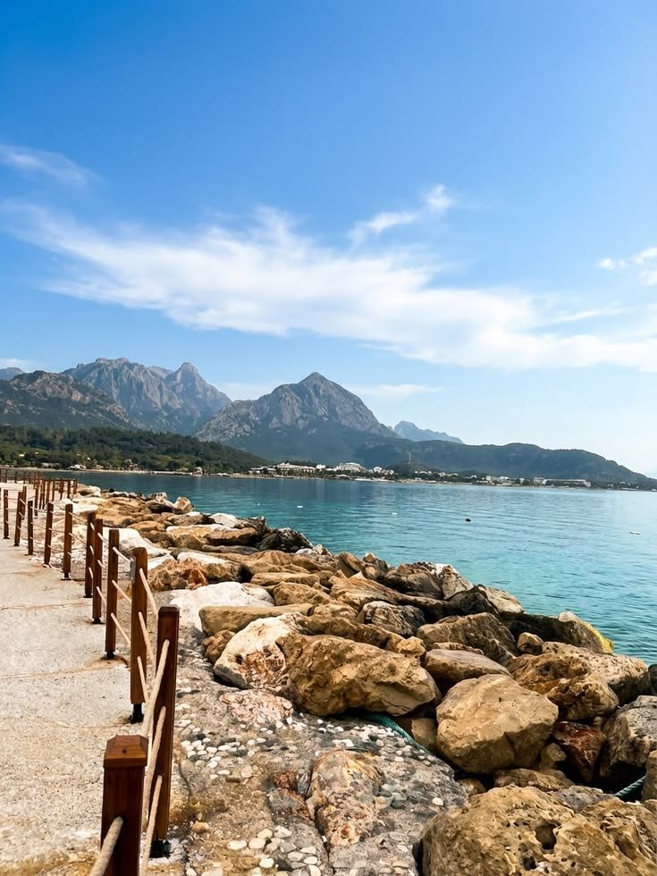 Rope rails beside a rocky shoreline path with mountains across the bay at NG Phaselis Bay.