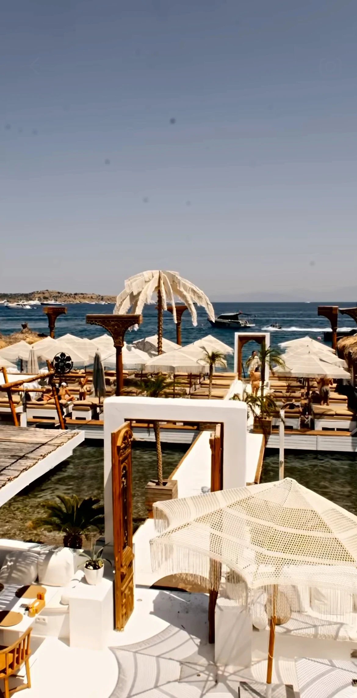 The Dimare Palm Tree seen across the Reana Beach deck, framed by carved timber doorways and a parasol