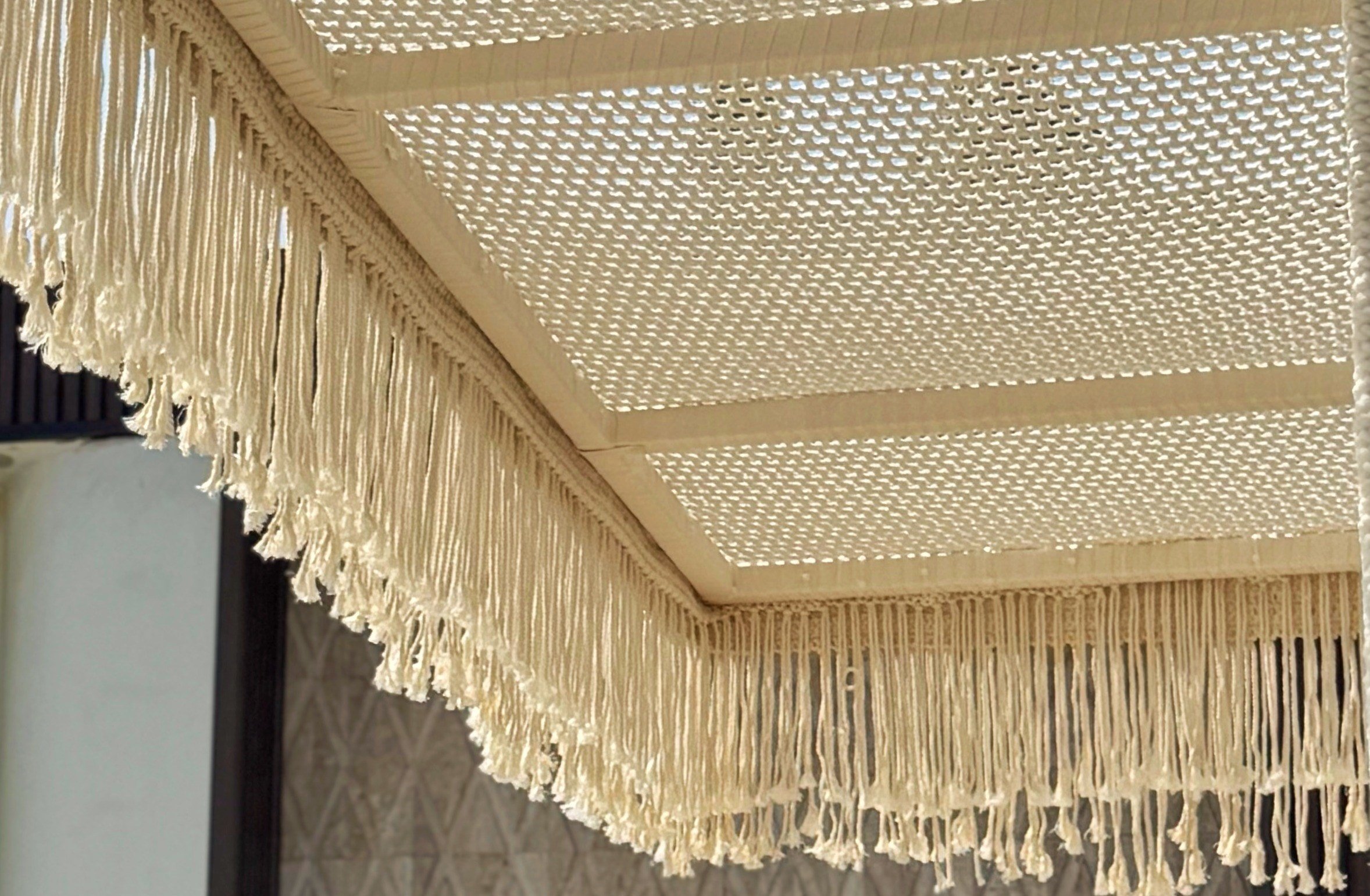 Knotted fringe along the edge of the ceiling panel system