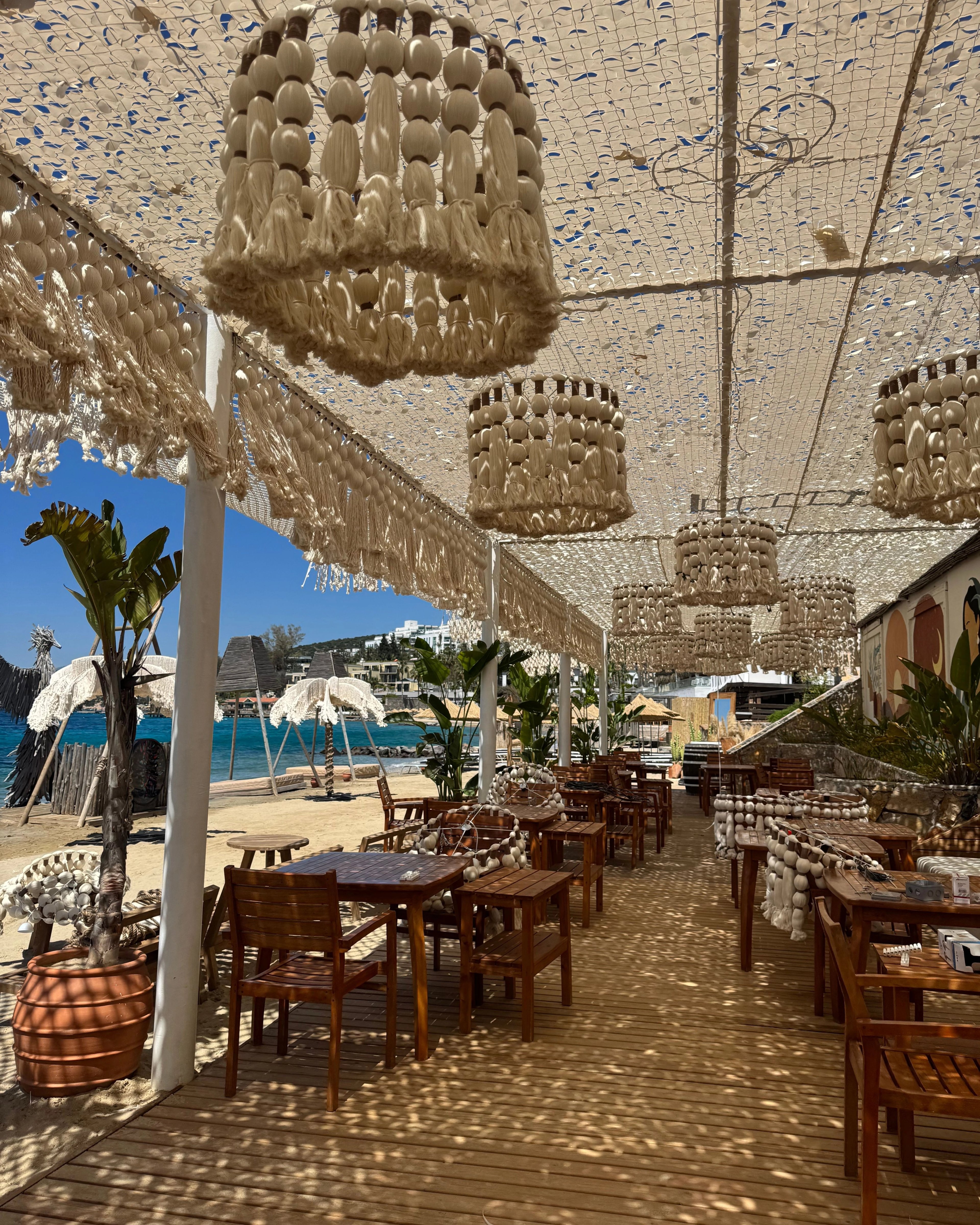 Hand-knotted open-mesh shade canopy over a beach restaurant terrace, with woven pendant lights