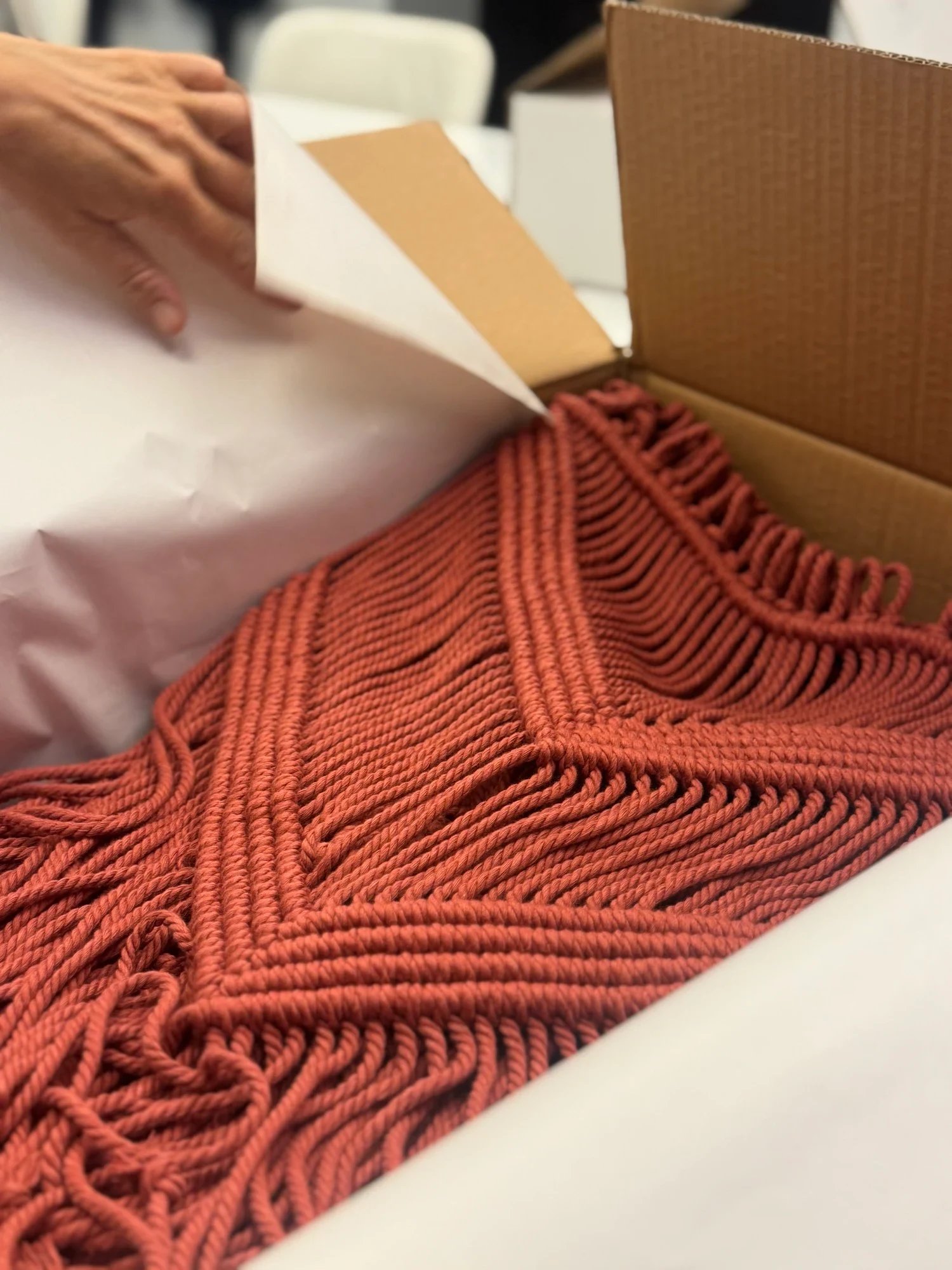 A terracotta knotted textile being wrapped inside a cardboard box.