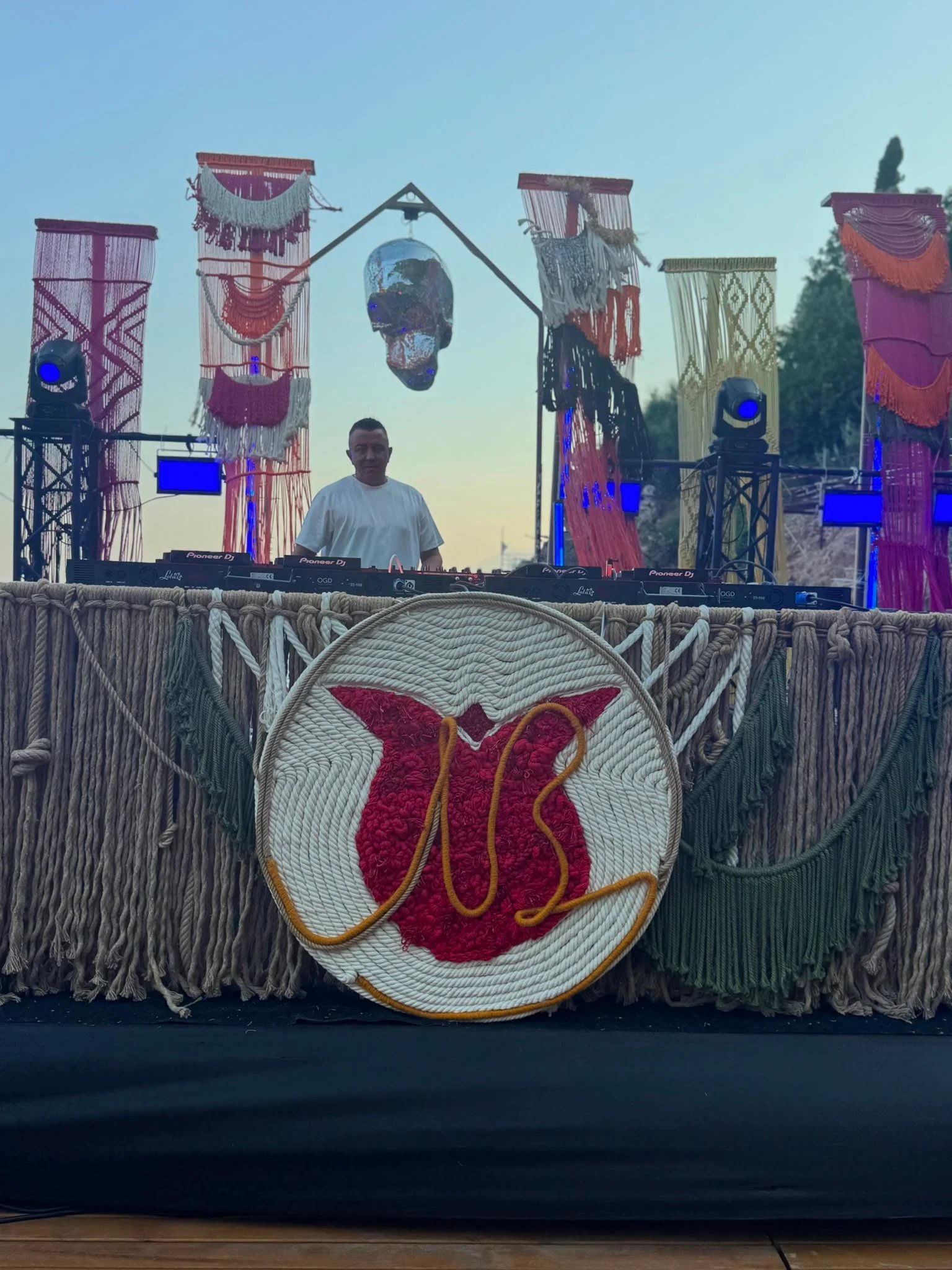The Dimare hand-knotted rope monogram medallion on the front of the DJ booth at Bilem Beach, banner columns behind