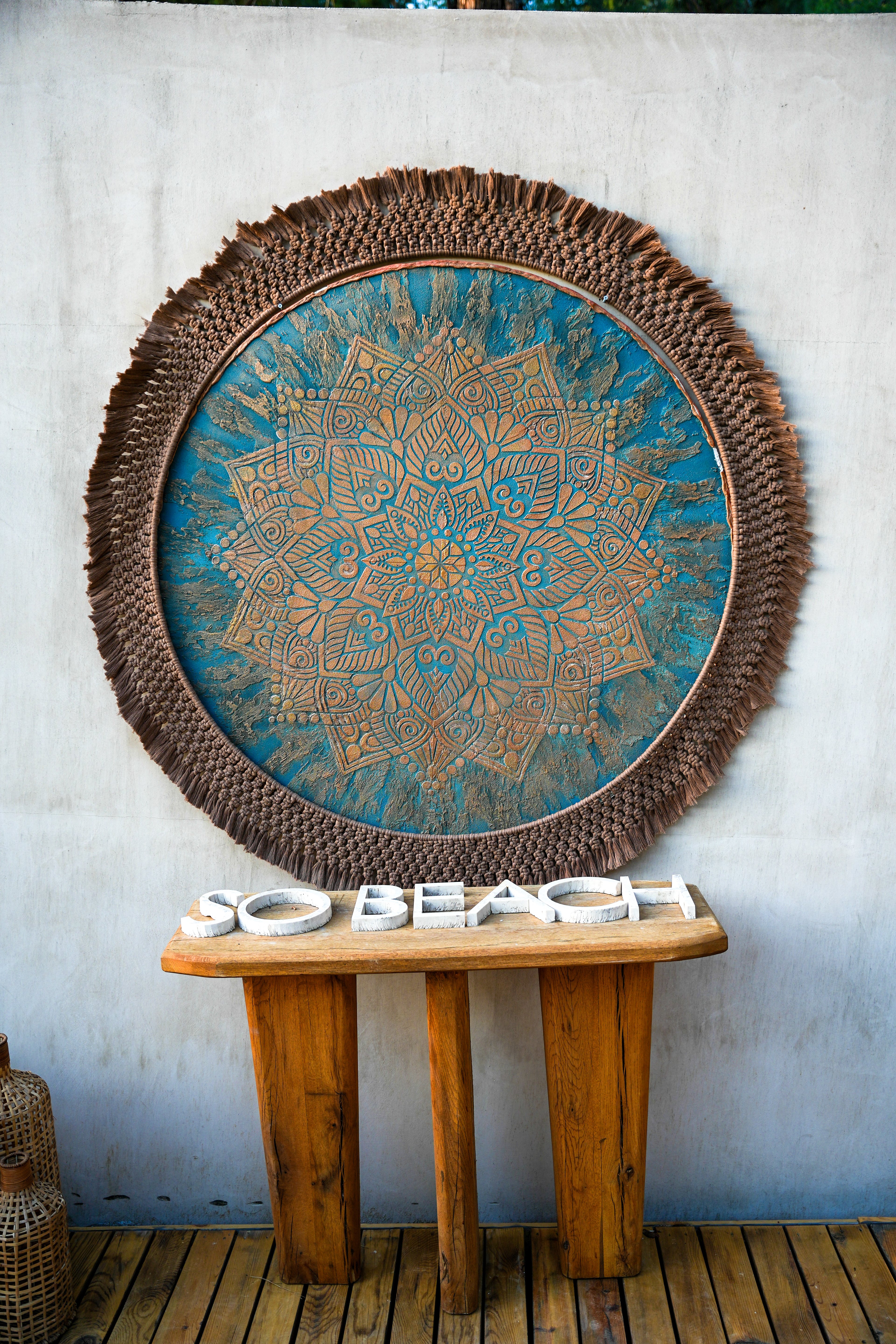 A circular blue patterned wall piece with a dark fringed border above a console and So Beach lettering.