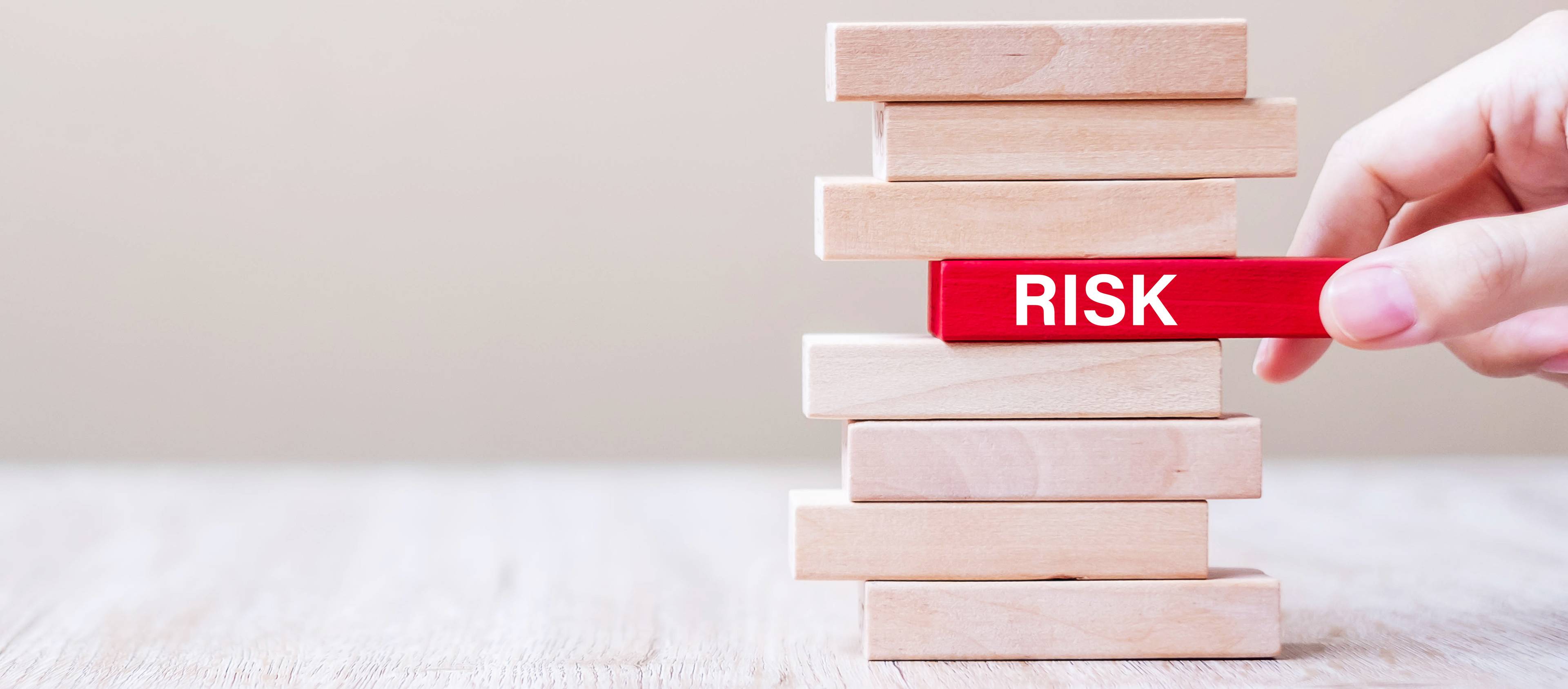 Pulling a wooden block with the word "RISK" from the middle of the stack