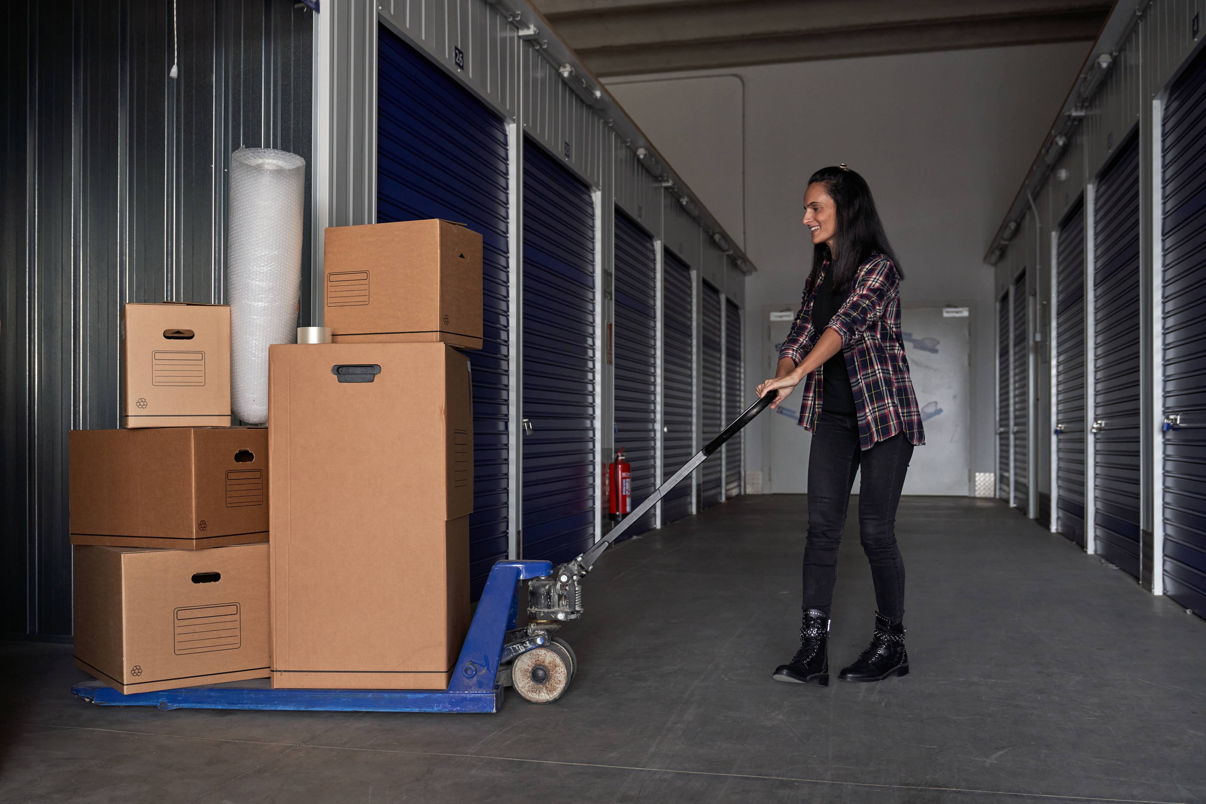 Woman pushing trolley full of boxes into a storage unit. 