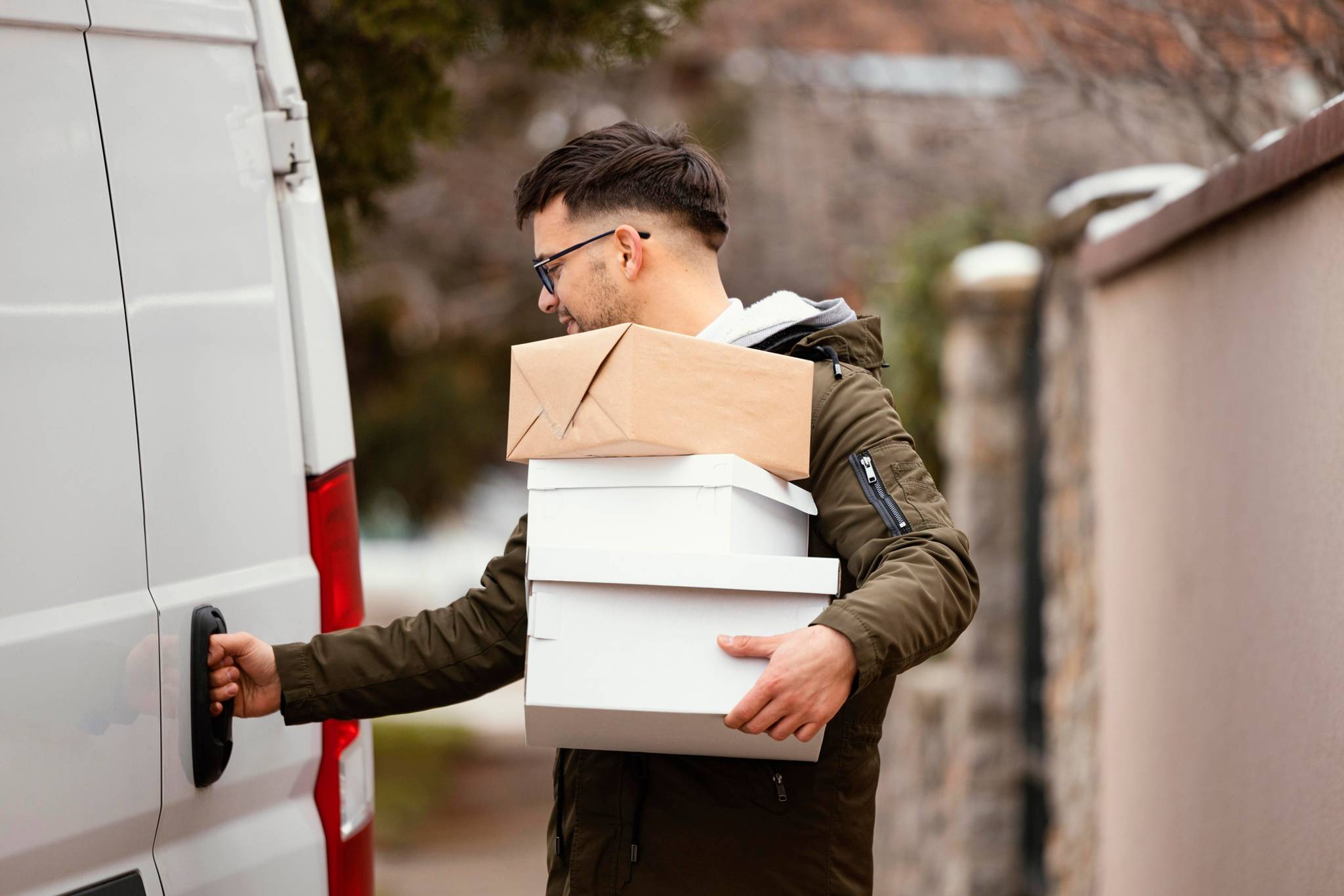 Man holding several boxes as he open delivery van door.