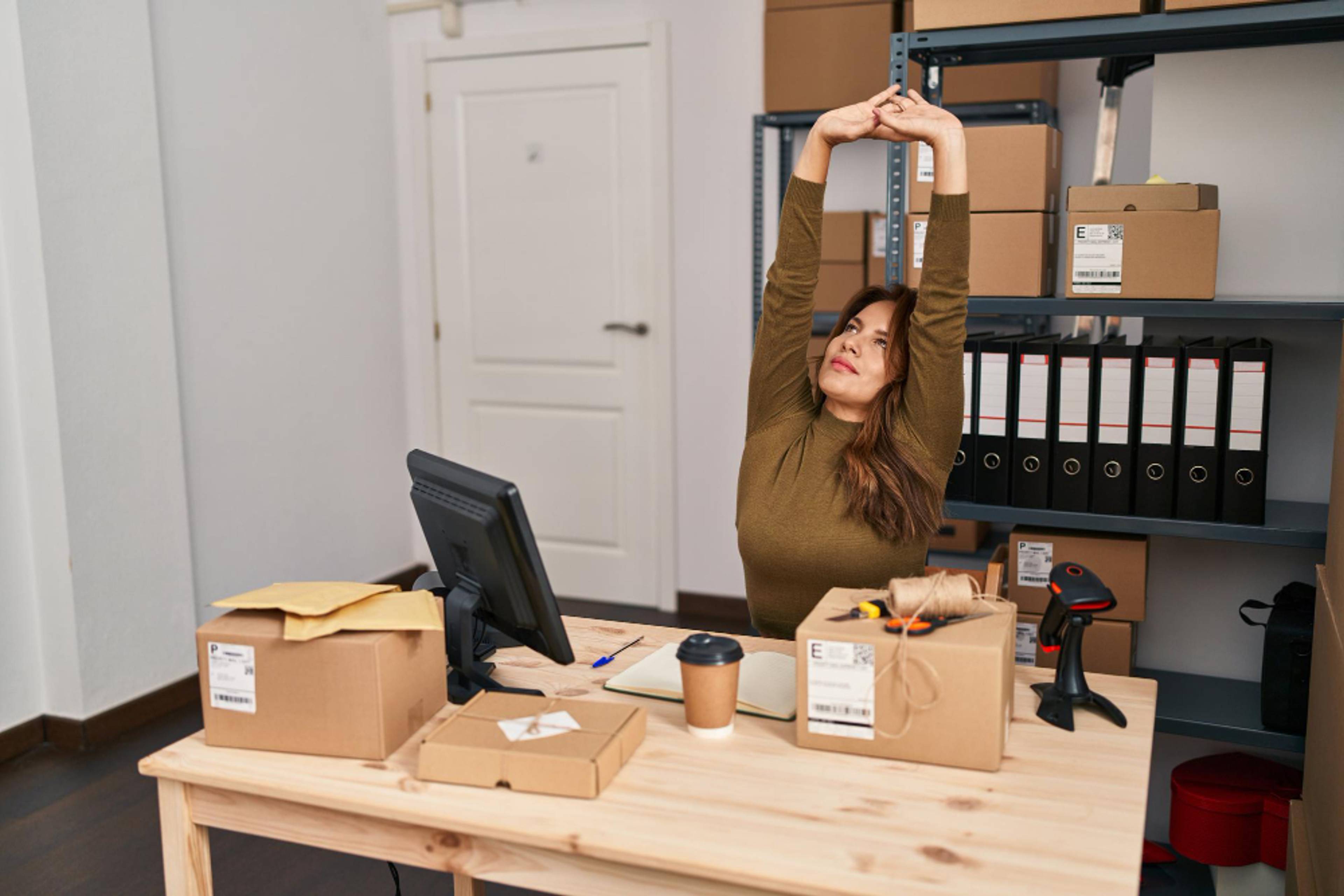 Woman stretching at a desk, in a closed off storage room