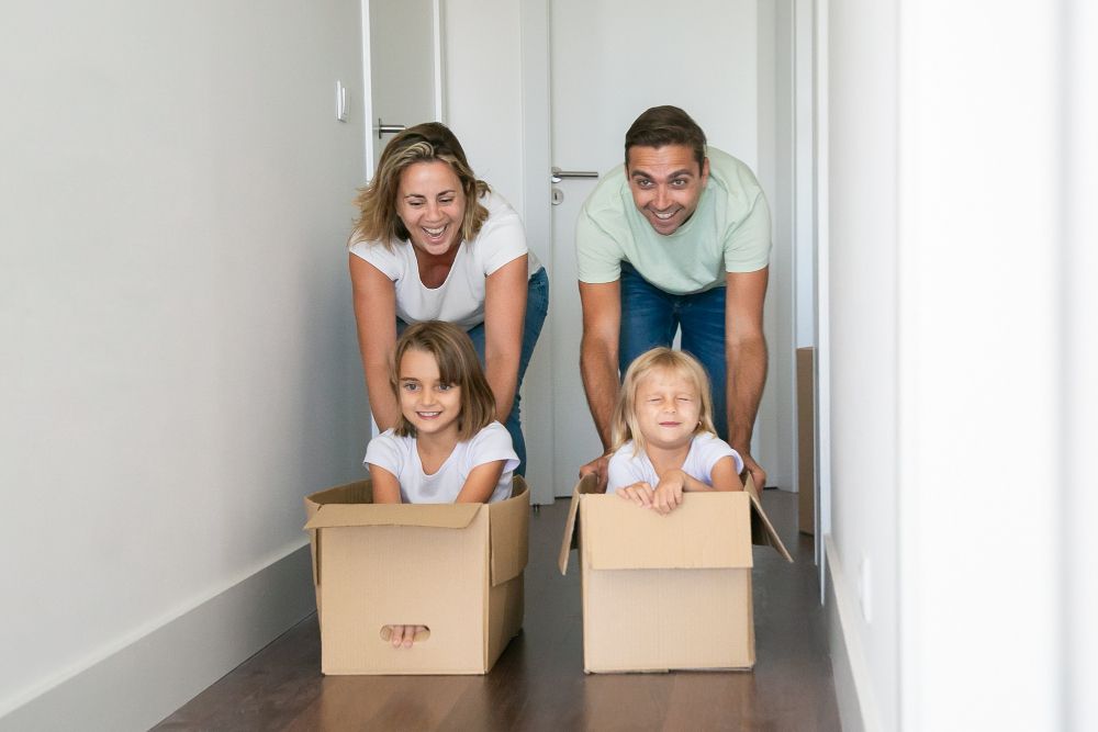 parents with two kids in boxes in new house hallway