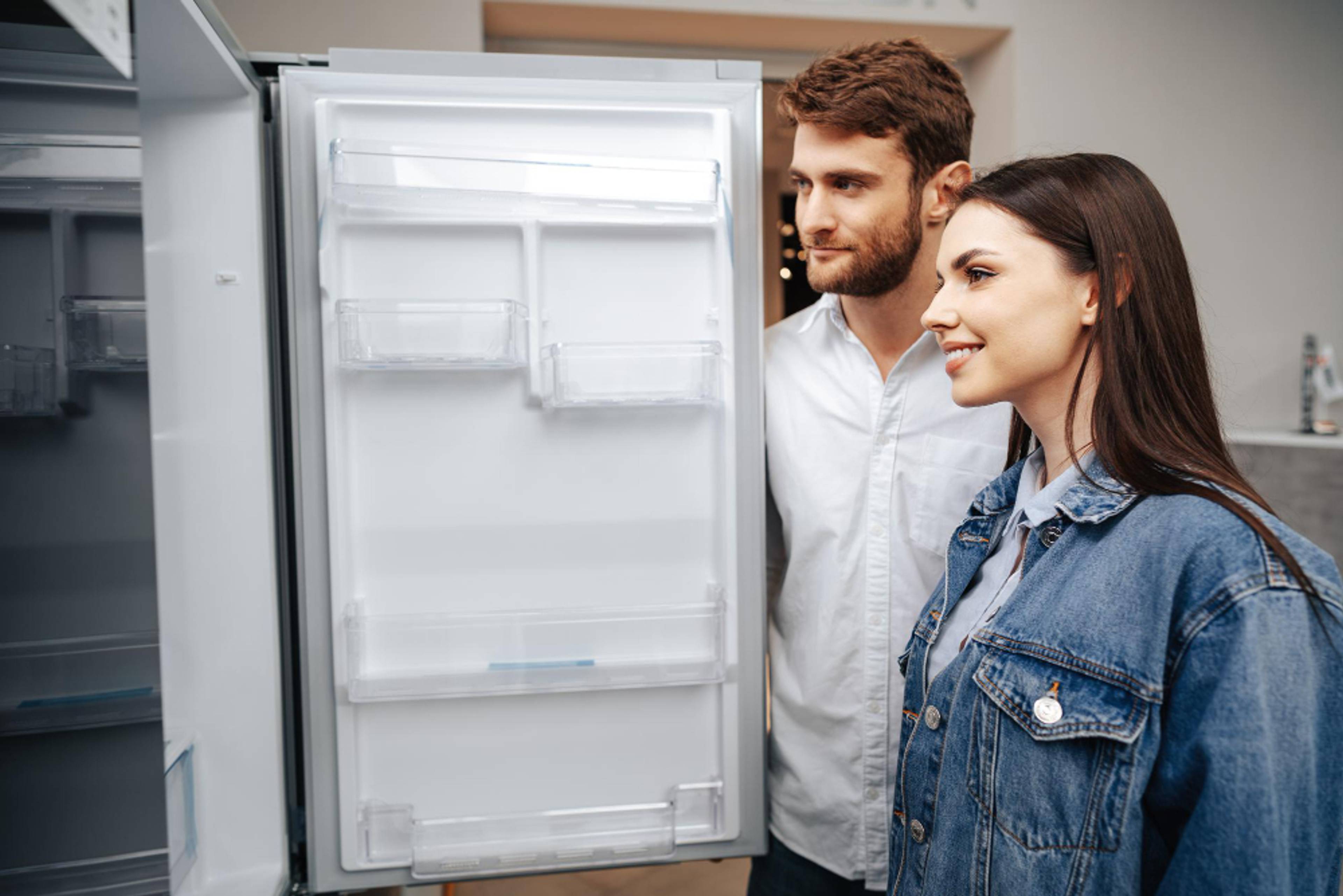 A couple looking into an empty fridge in their kitchen.