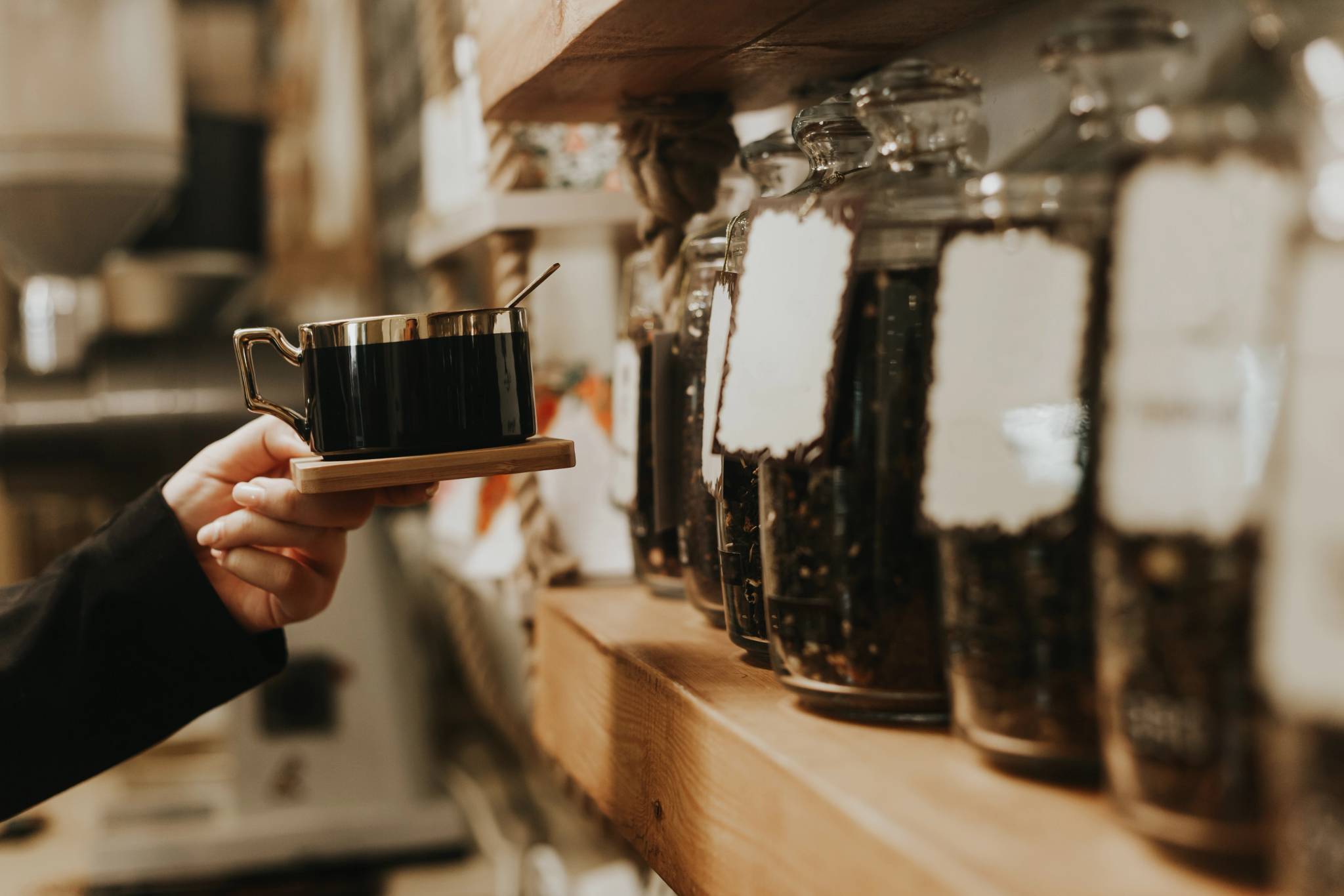 Female hand holding coffee cup in coffee shop in front of shelves