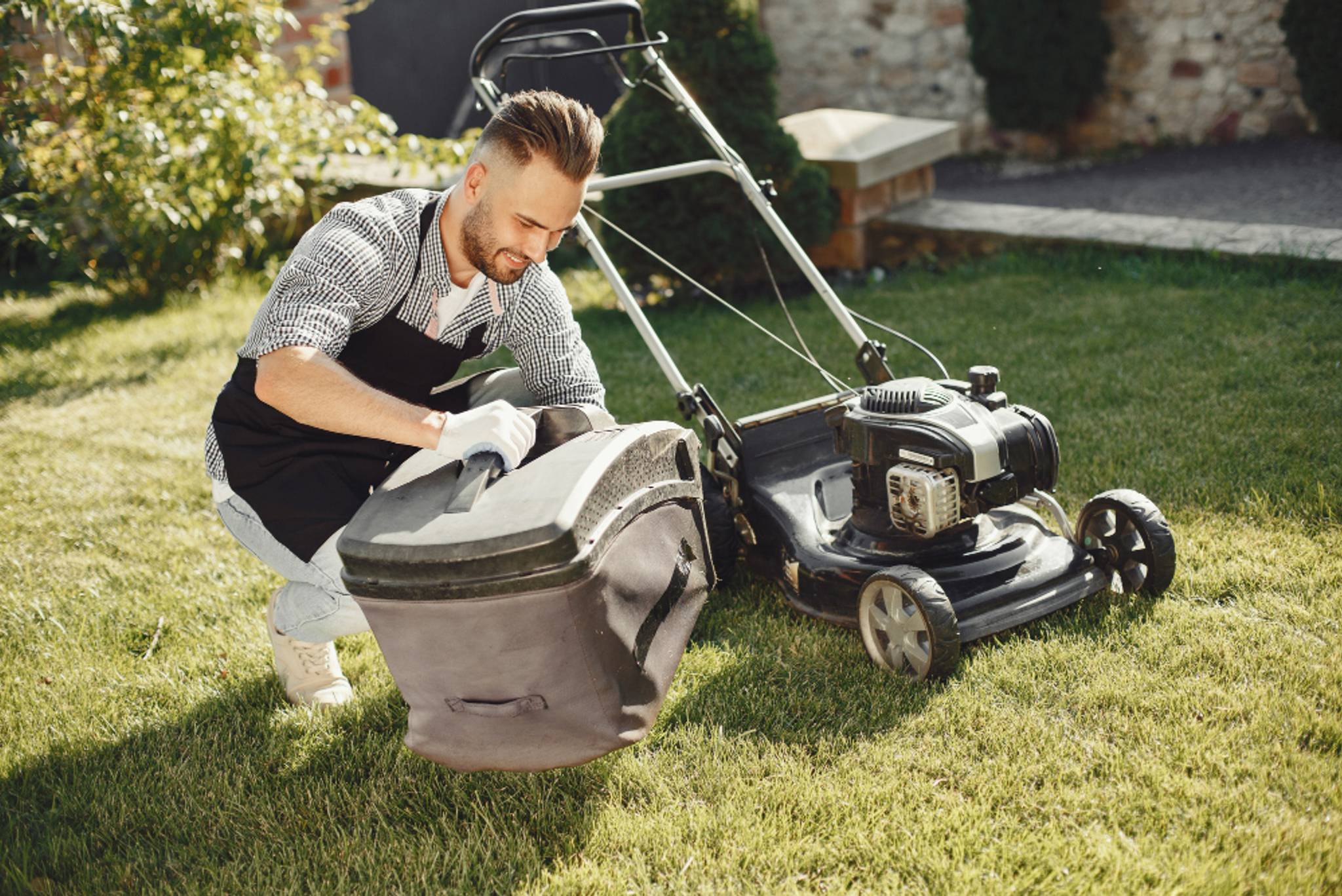 A person emptying their lawn mower and cleaning out the back part of any grass