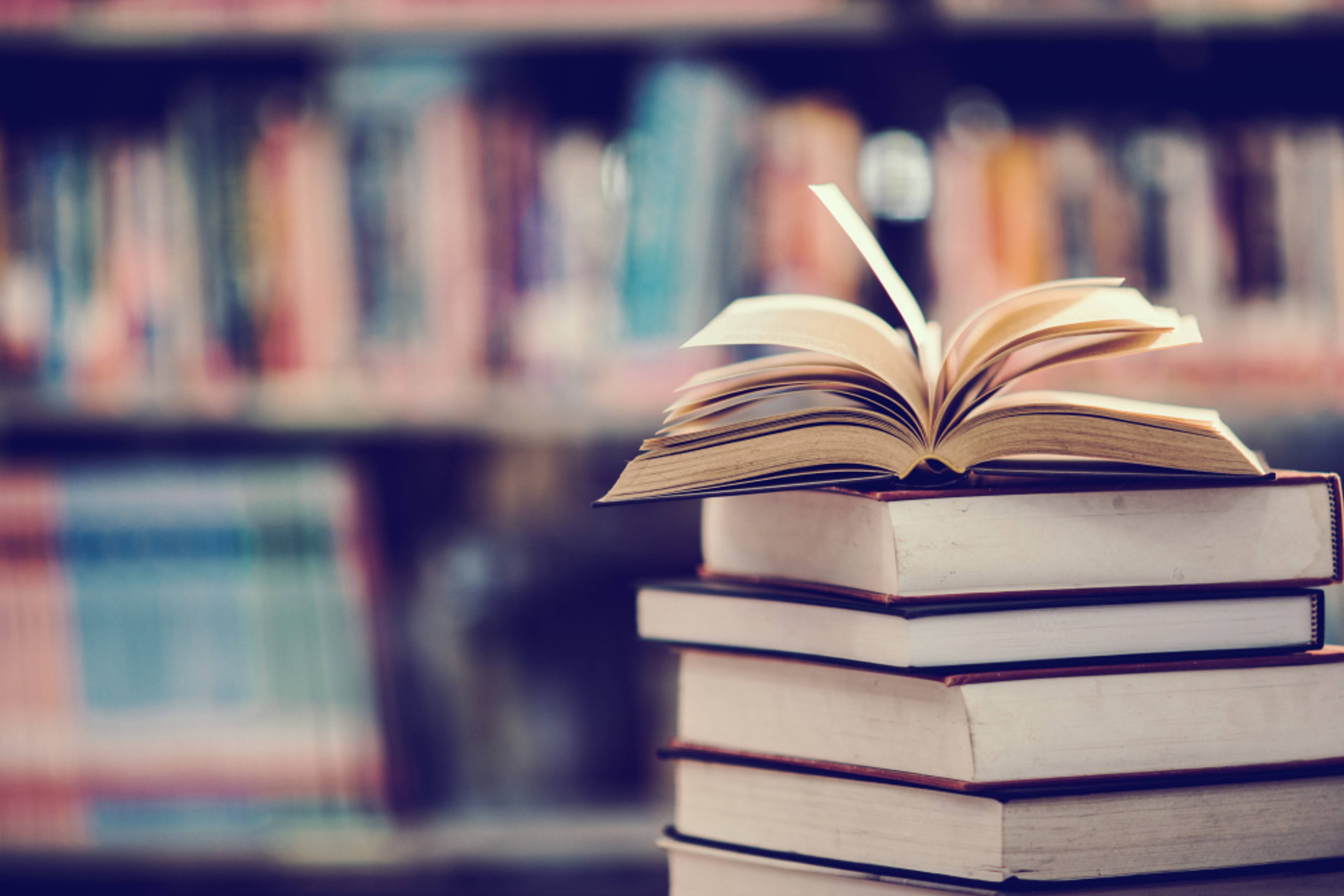 A pile of books in a library with a book open on top