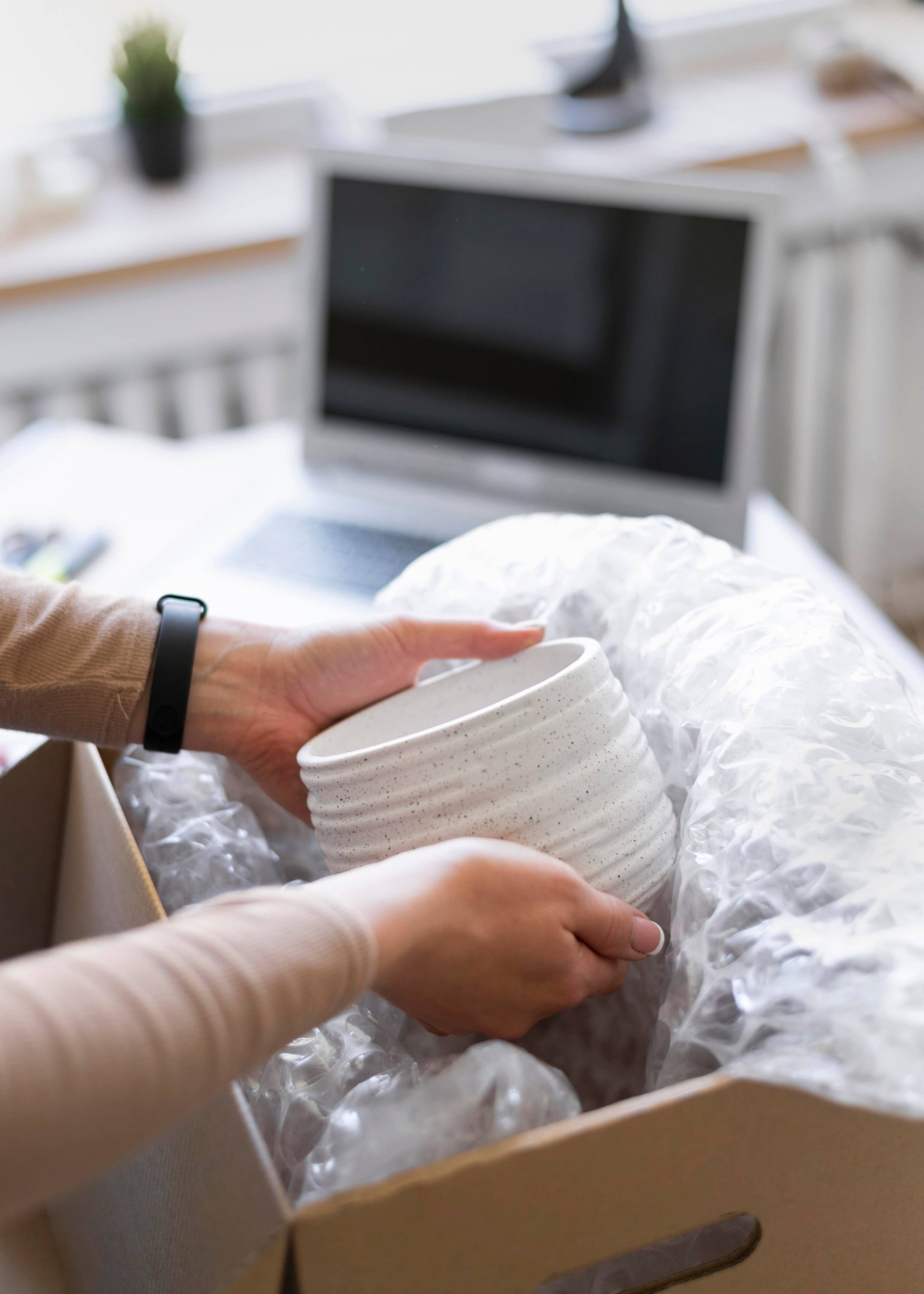 Close up photo of hands packing away bowls in a cardboard box with bubble wrap.
