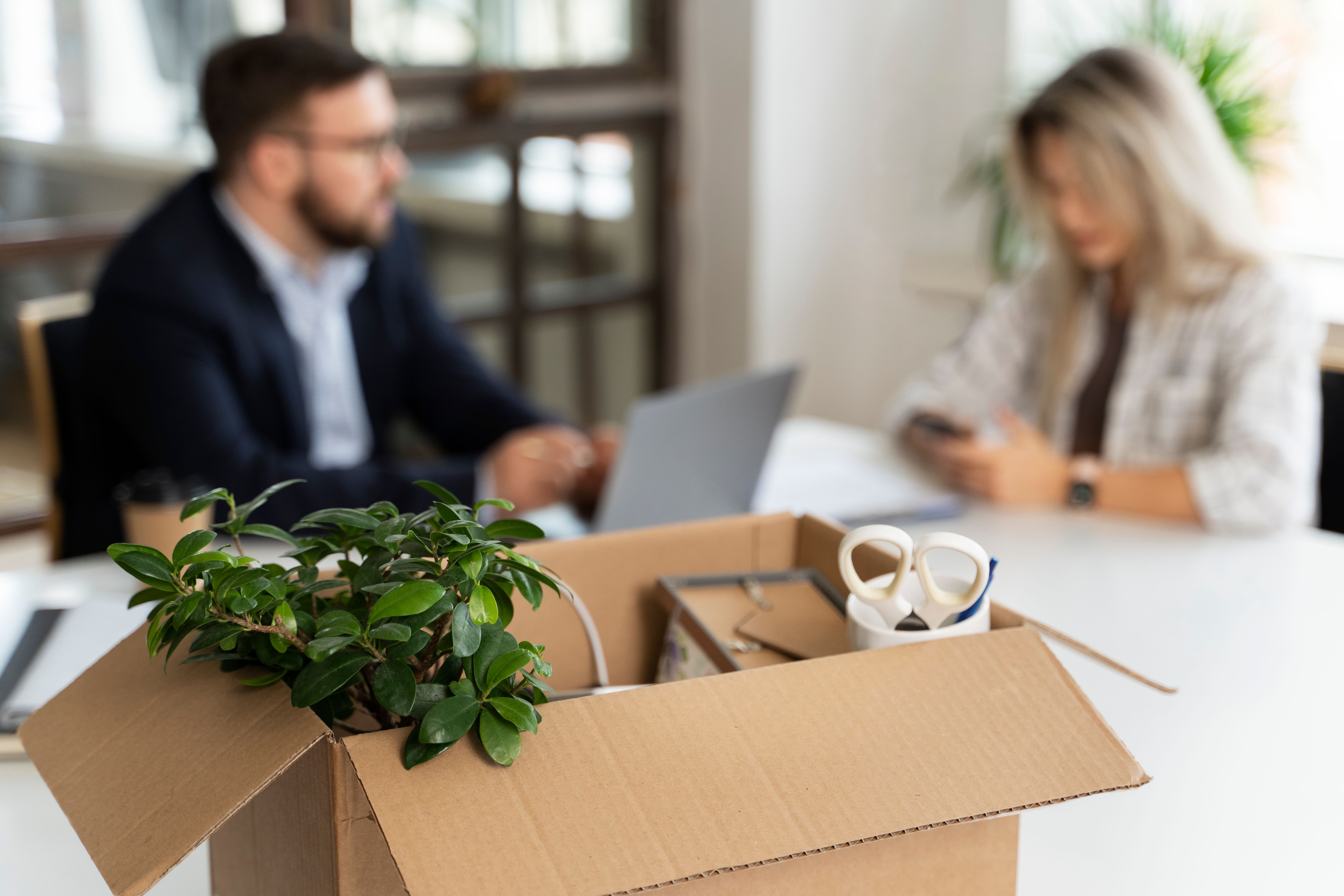 box with in foreground with 2 office workers in background