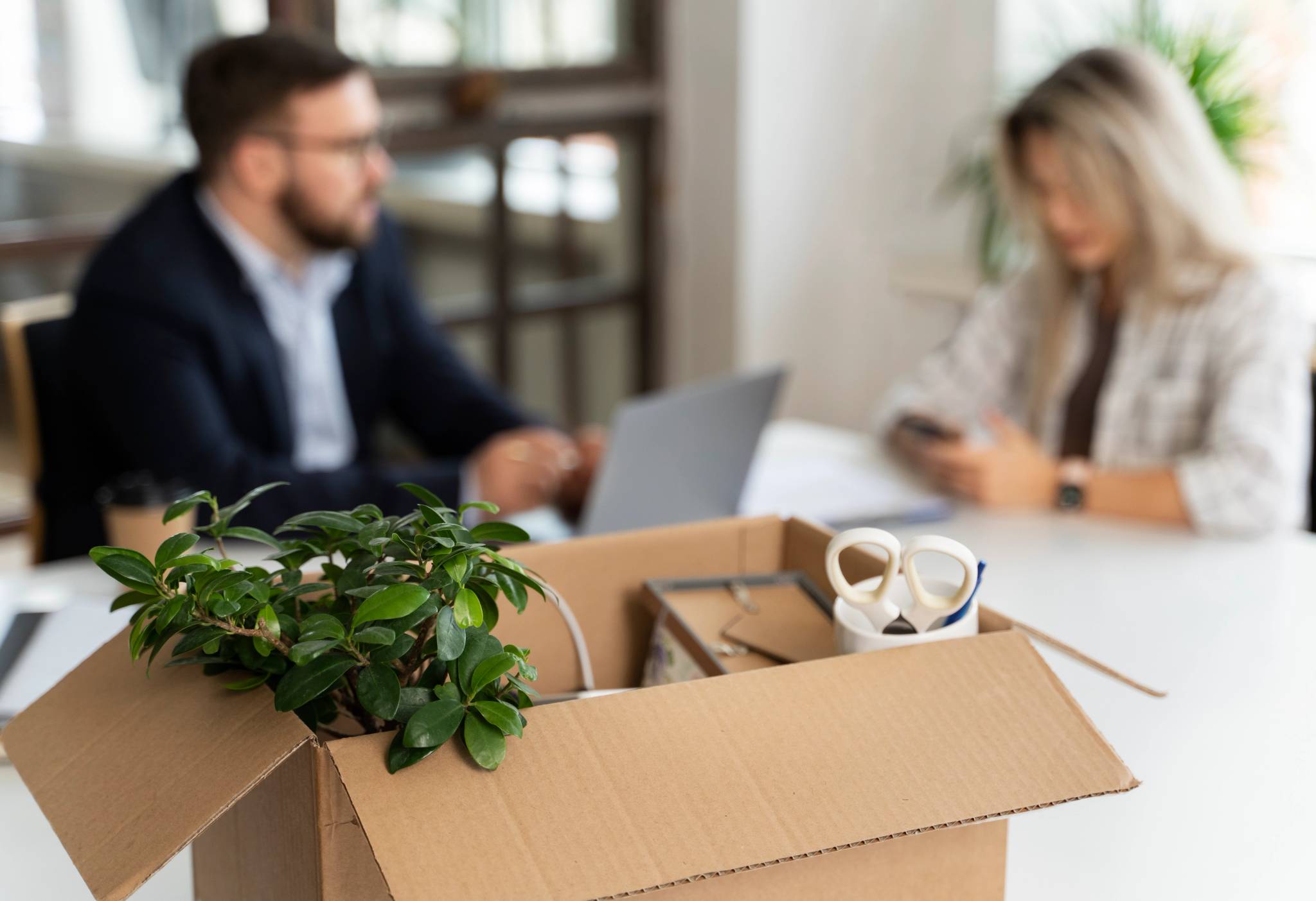 box with in foreground with 2 office workers in background