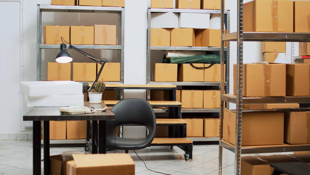 A desk and chair surrounded by shelving units filled with boxes.