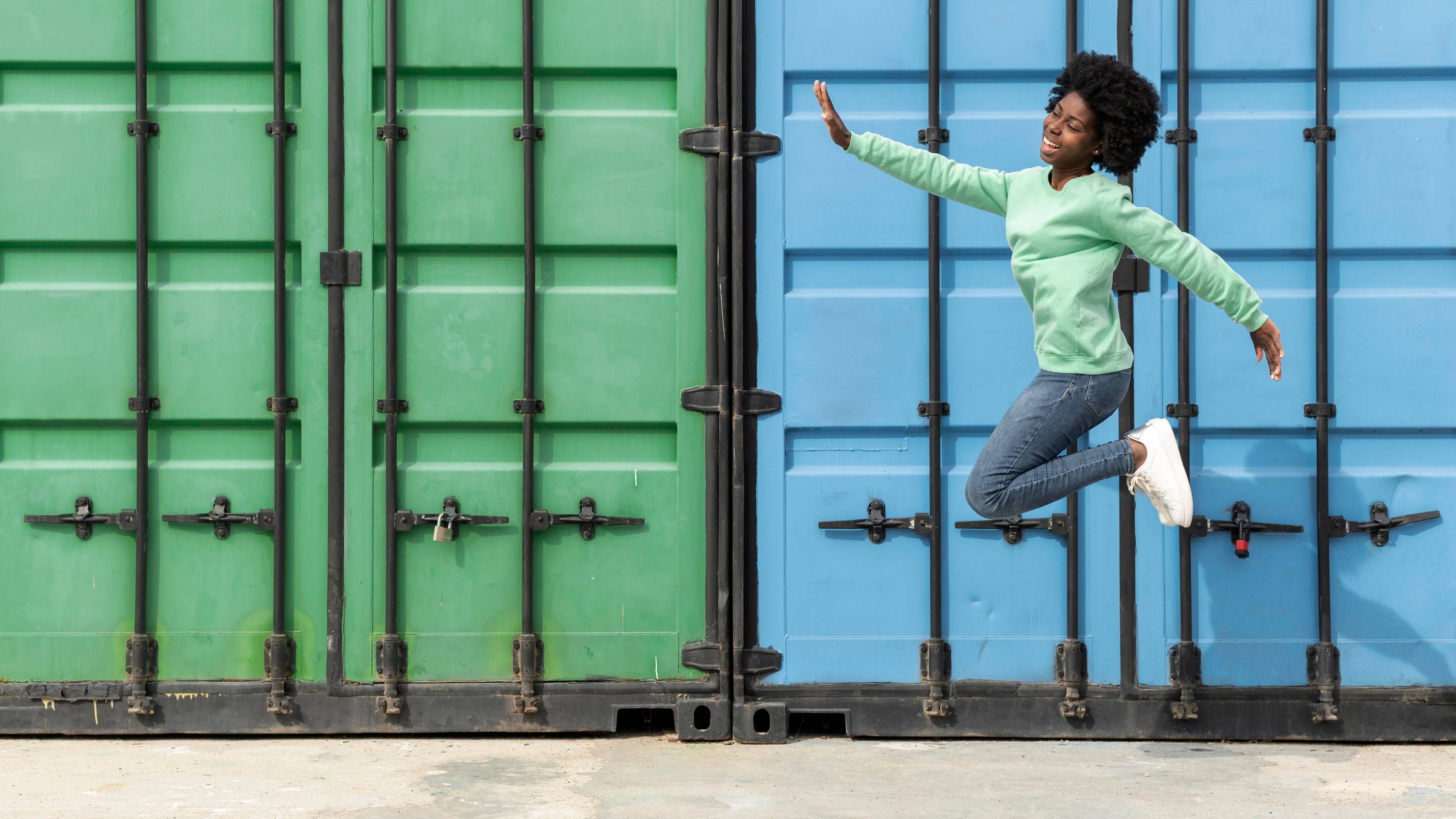 Young woman jumping in front of container storage.