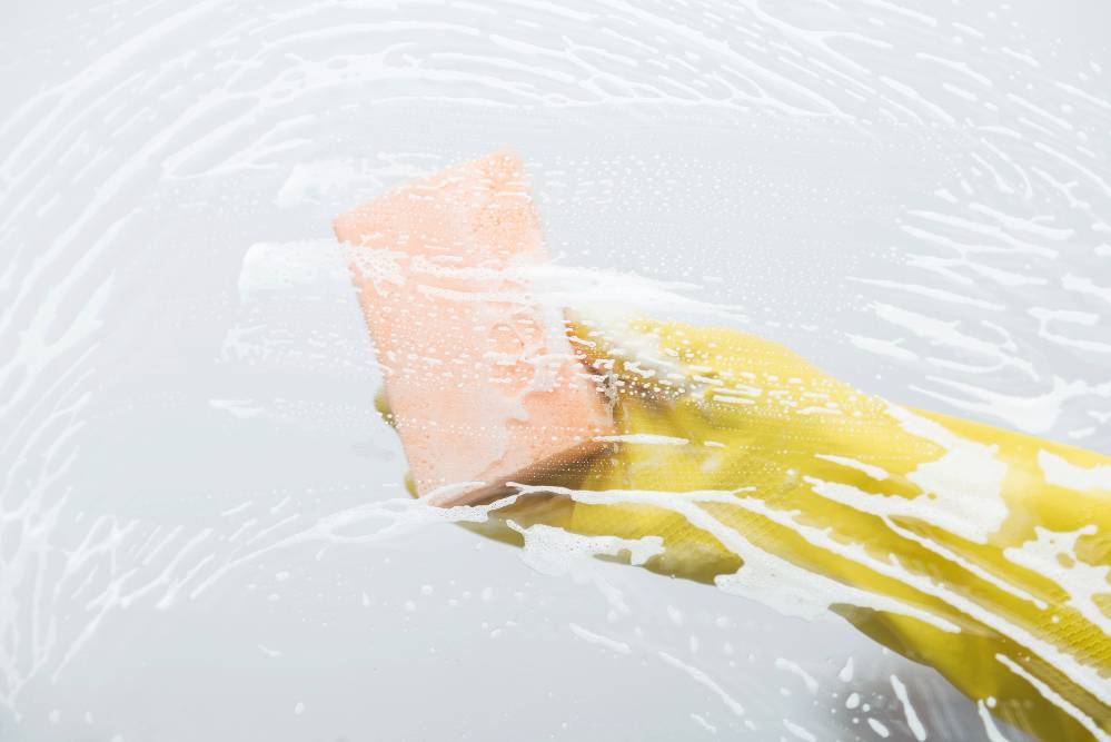 A yellow gloved hand cleans a surface with a sponge