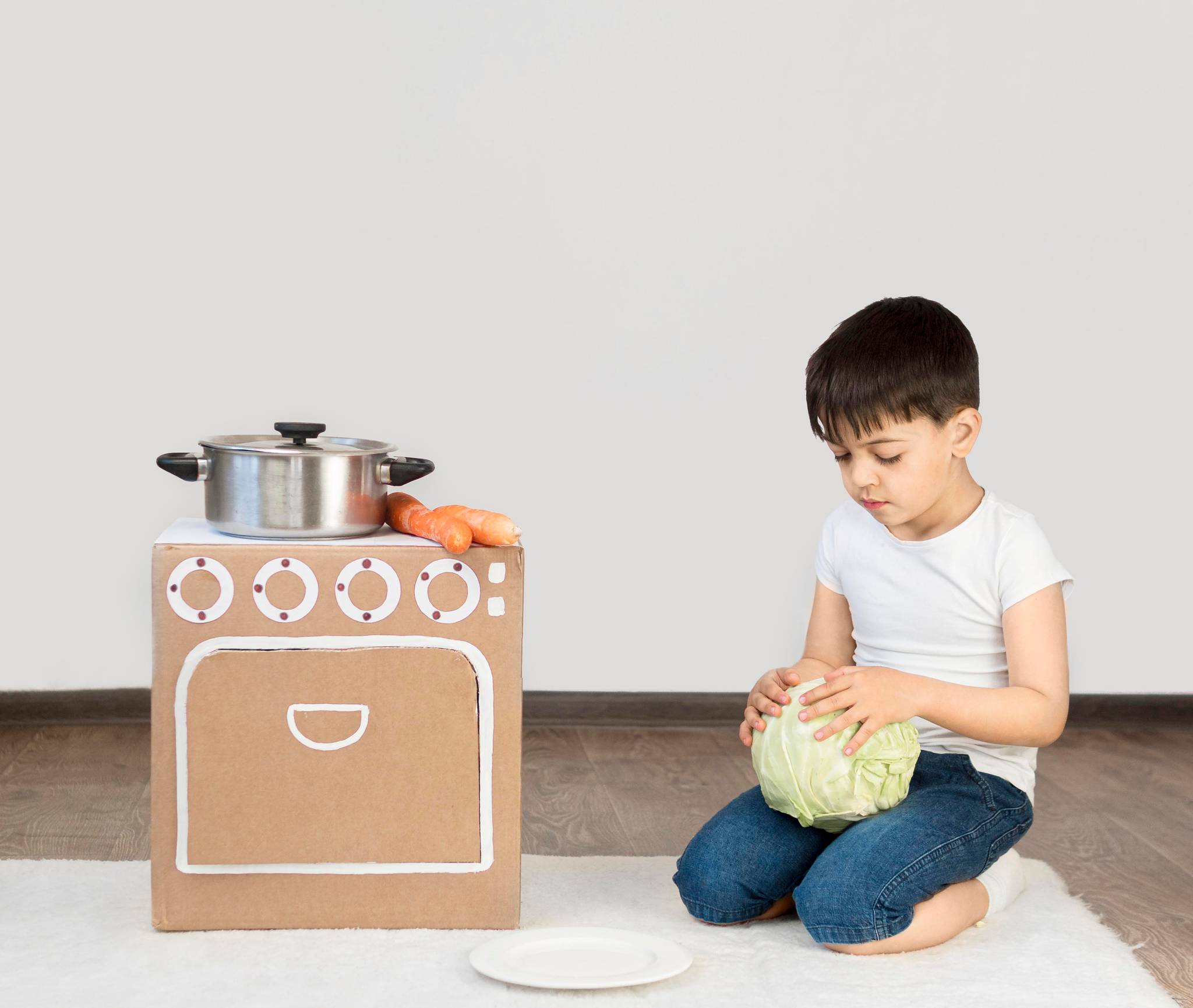 Kid holding a cabbage while playing with cardboard oven