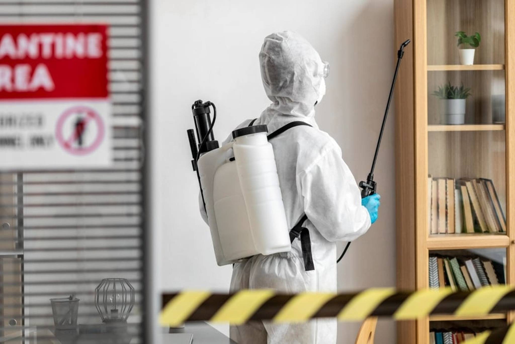 Person in white protective gear using chemicals to remove pests