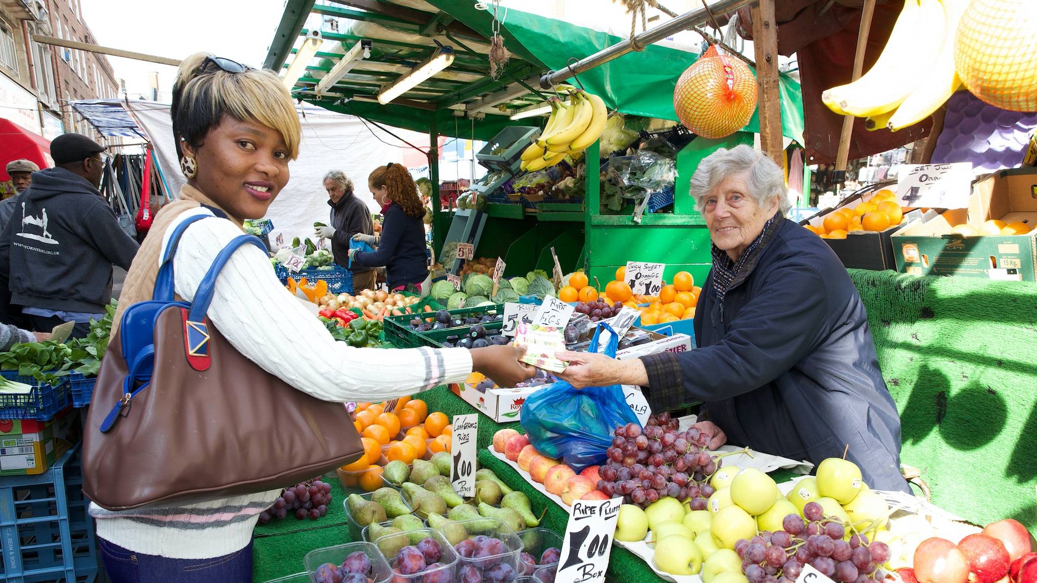 old lady fruit and veg trader smiling doing business with young lady