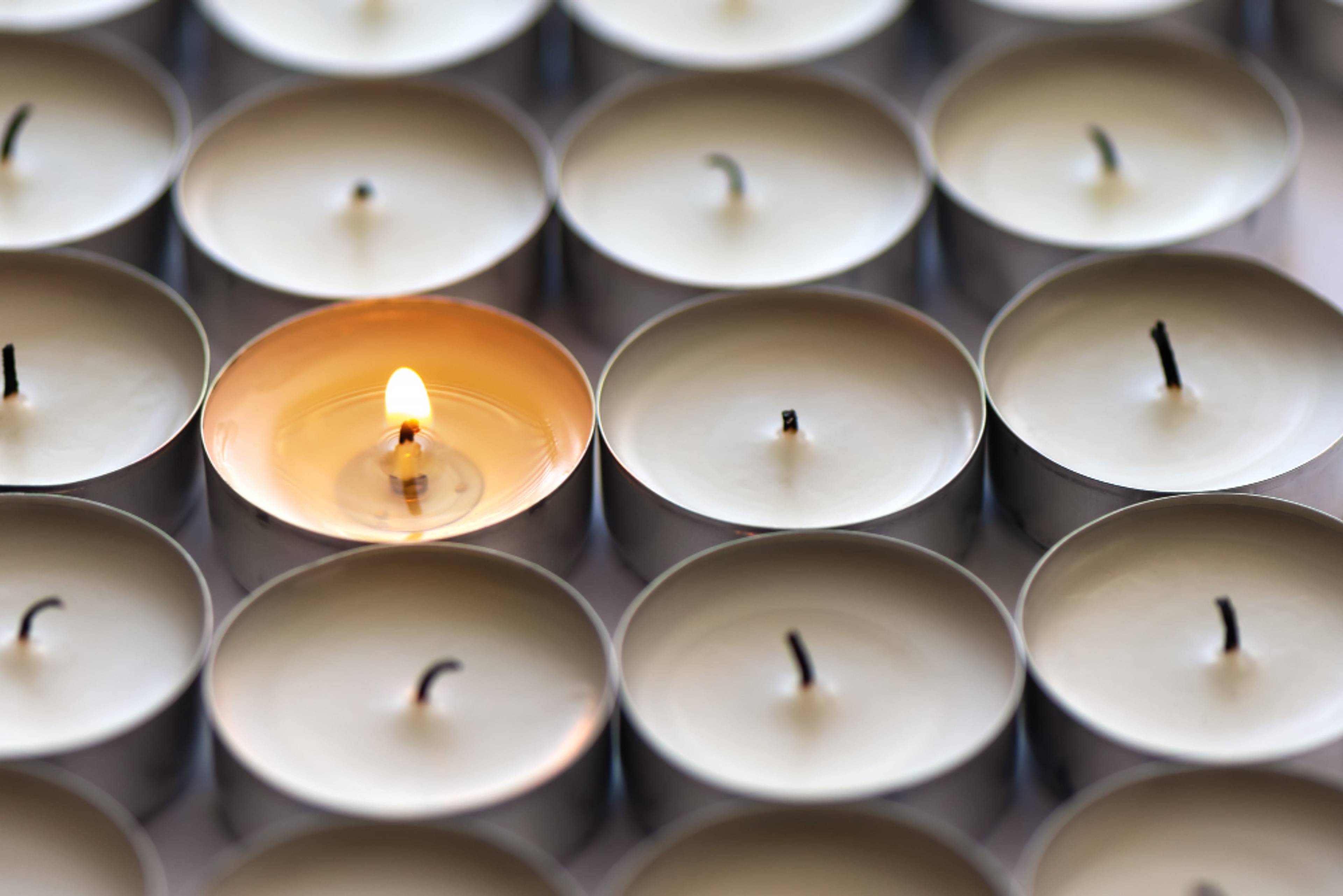 rows of small tea candles, one of them is lit