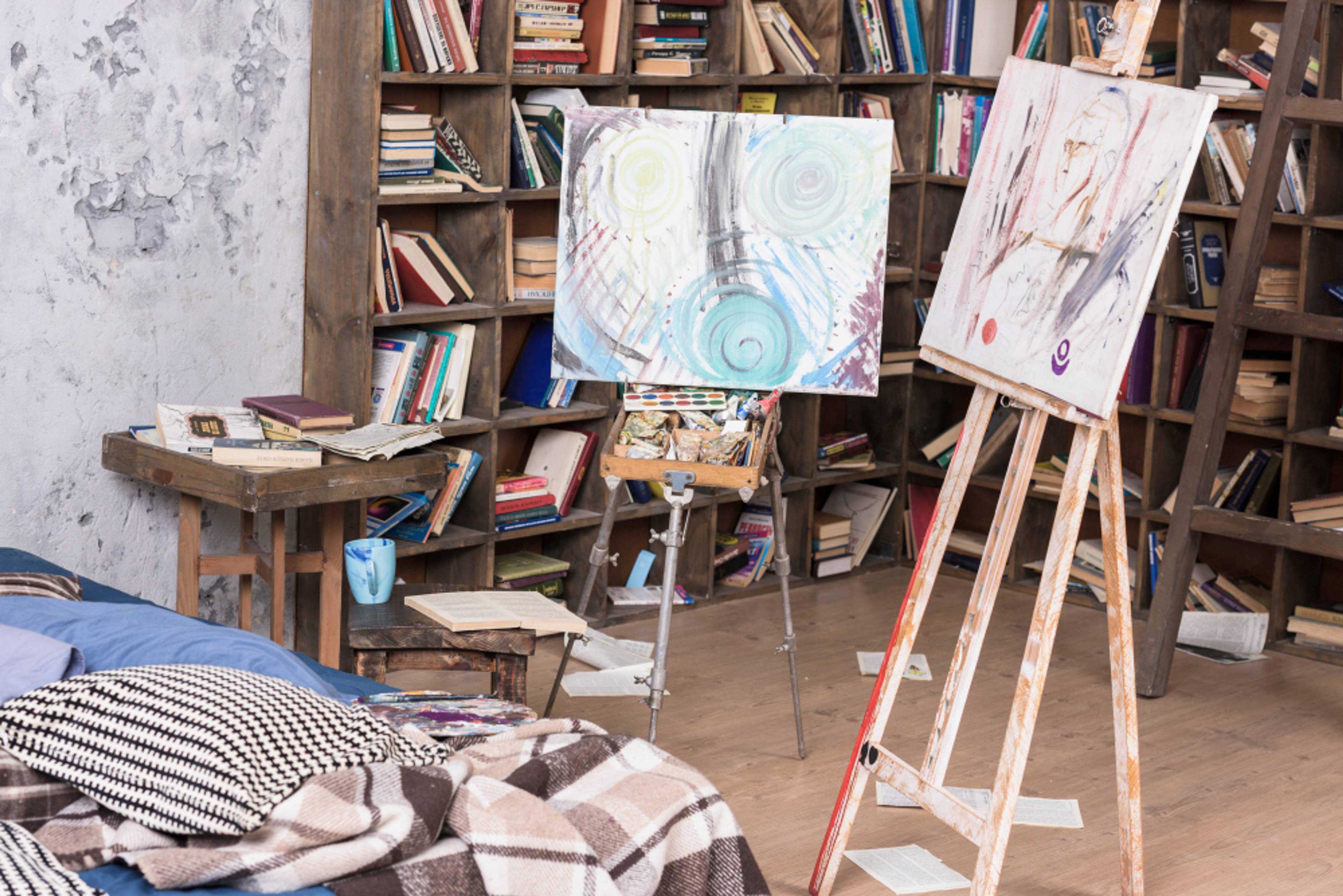 Two paintings on an easel in a room filled with books