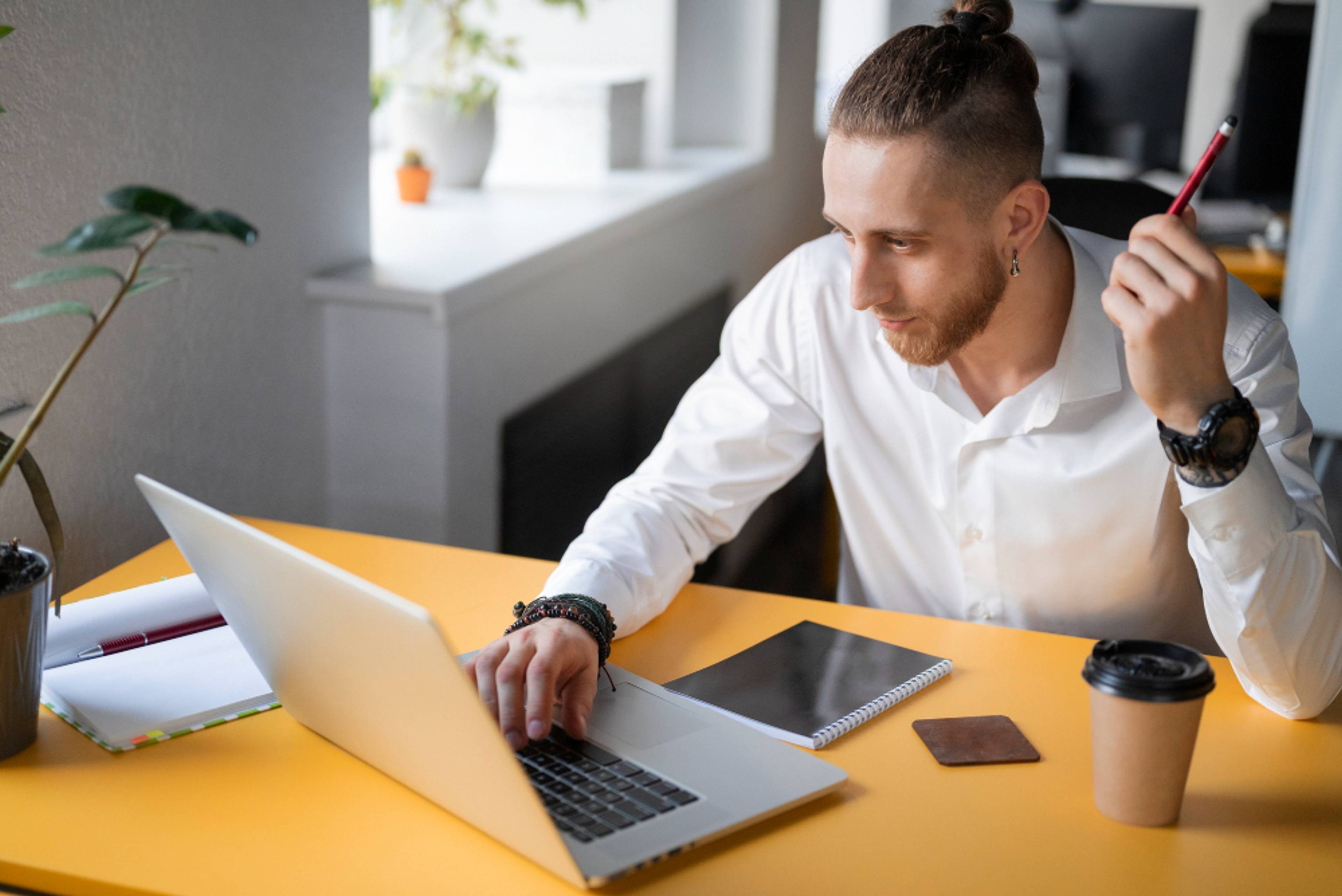 Man working on his computer at a yellow desk, looking satisfied