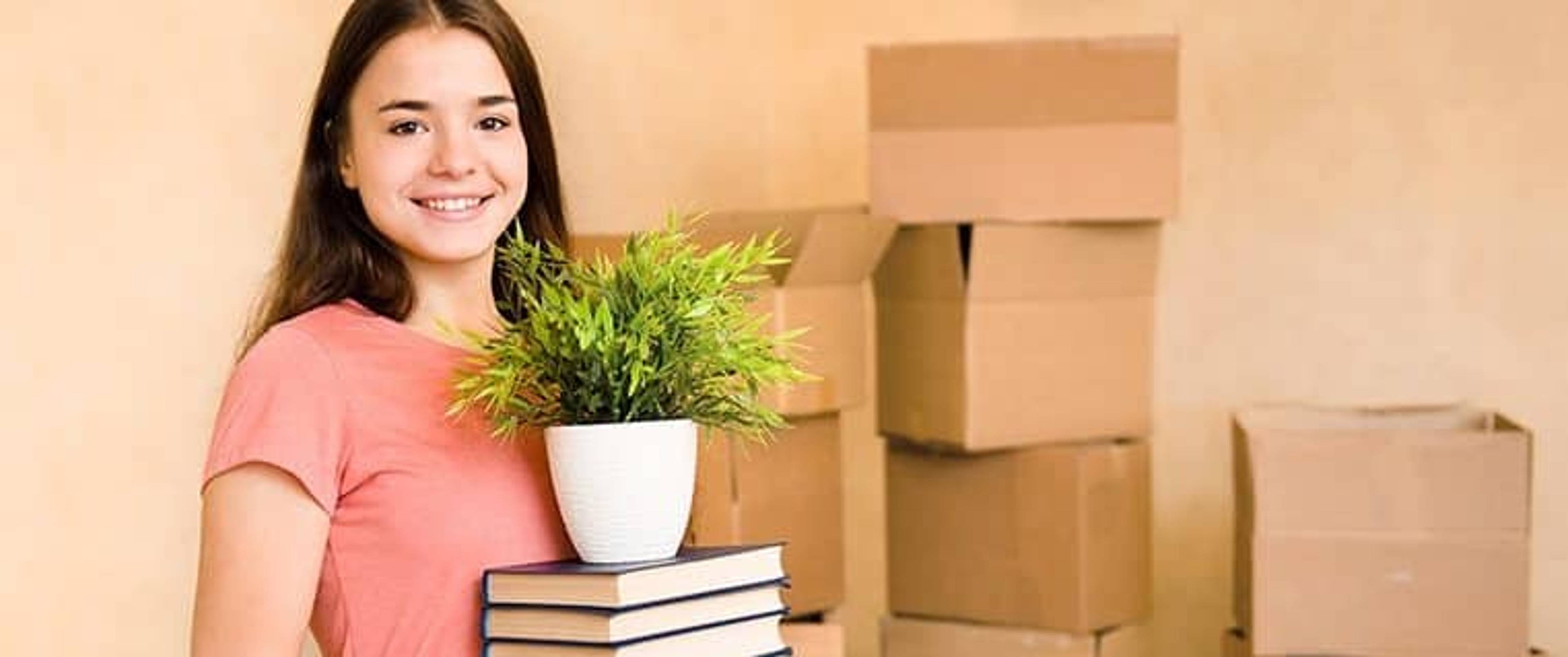 Women holding books and plant with boxes in background