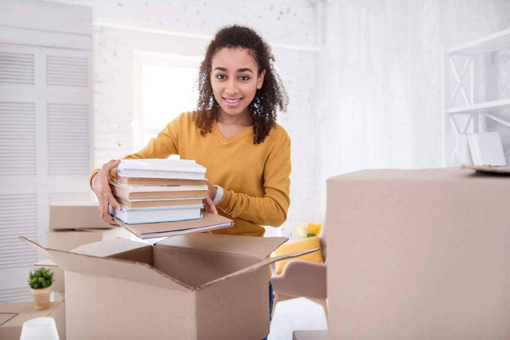 student smiling packing textbooks into cardboard box
