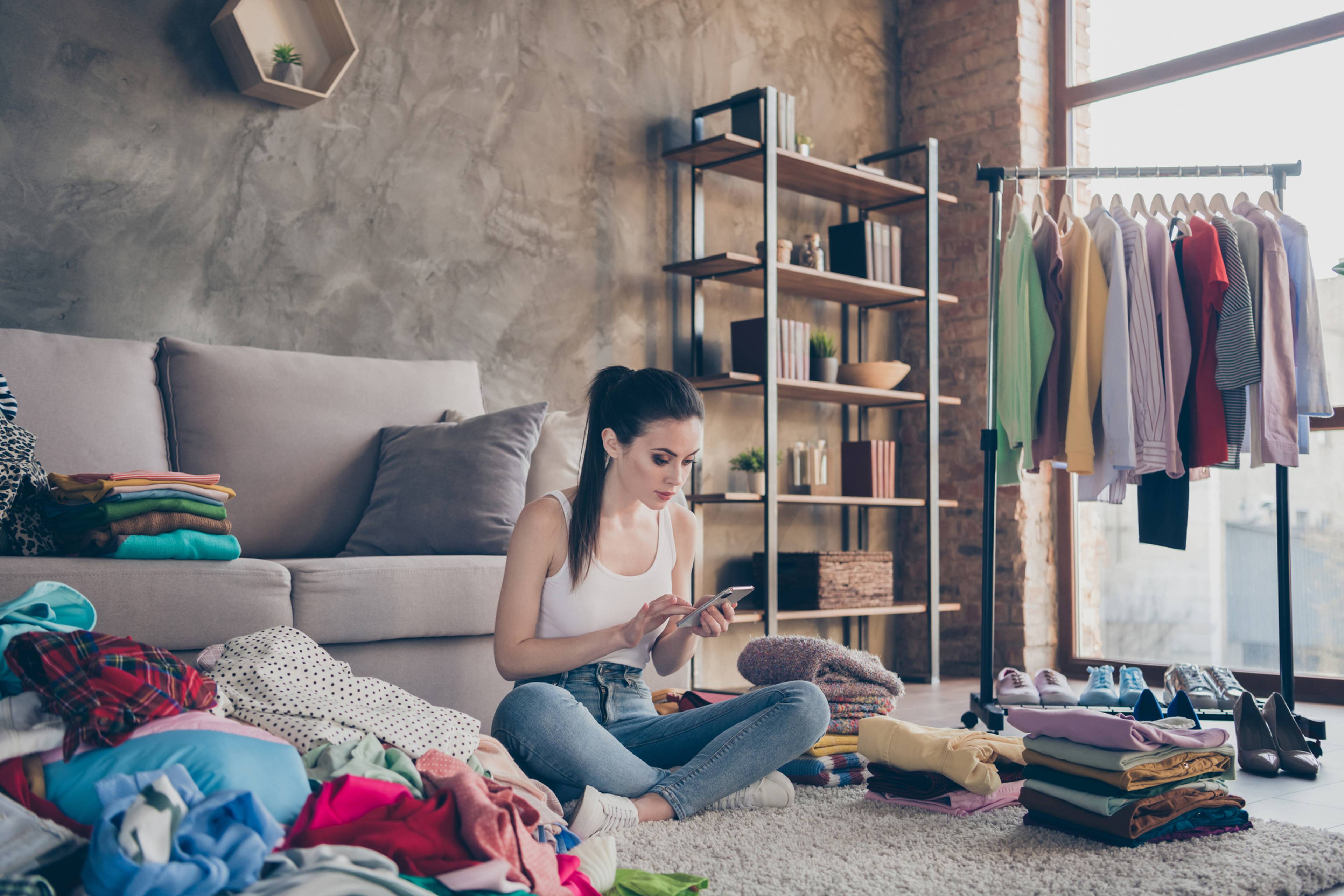 Woman on phone cross-legged on floor with clothes ready for sale