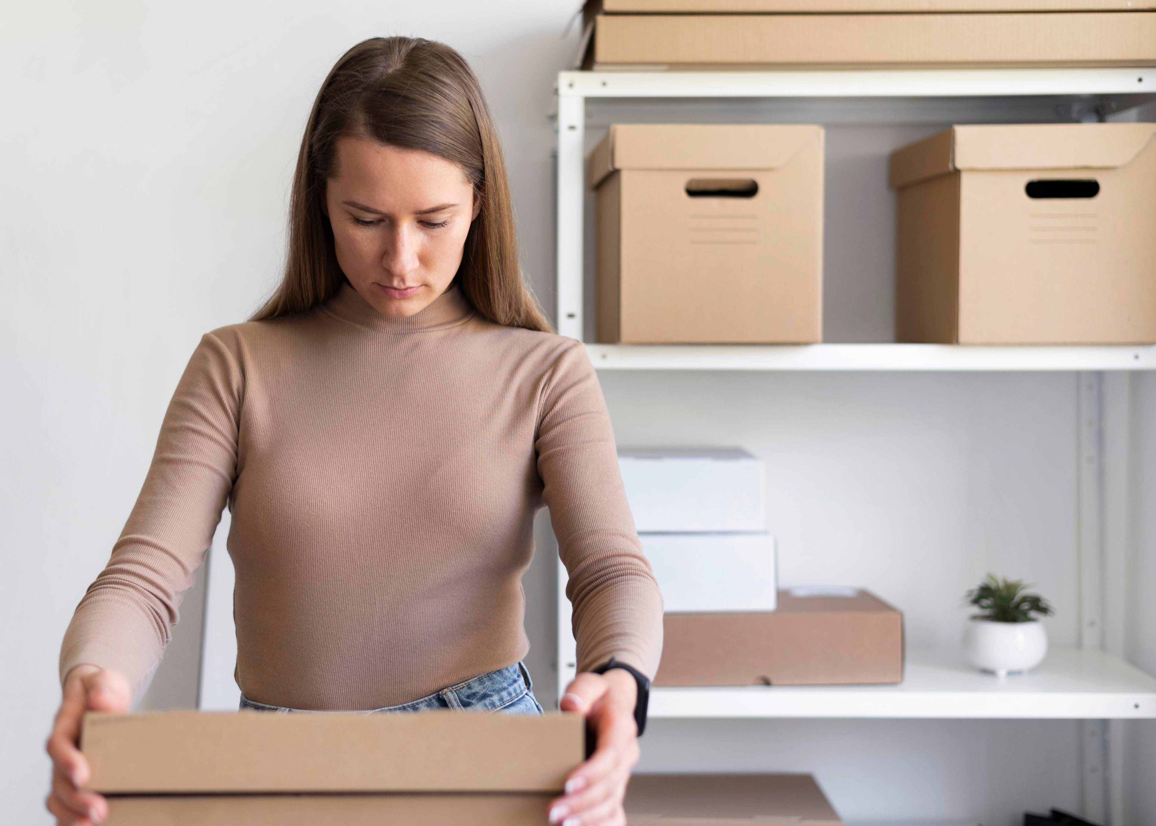 Woman fixing top of box with a couple of boxes on a shelf in the background.