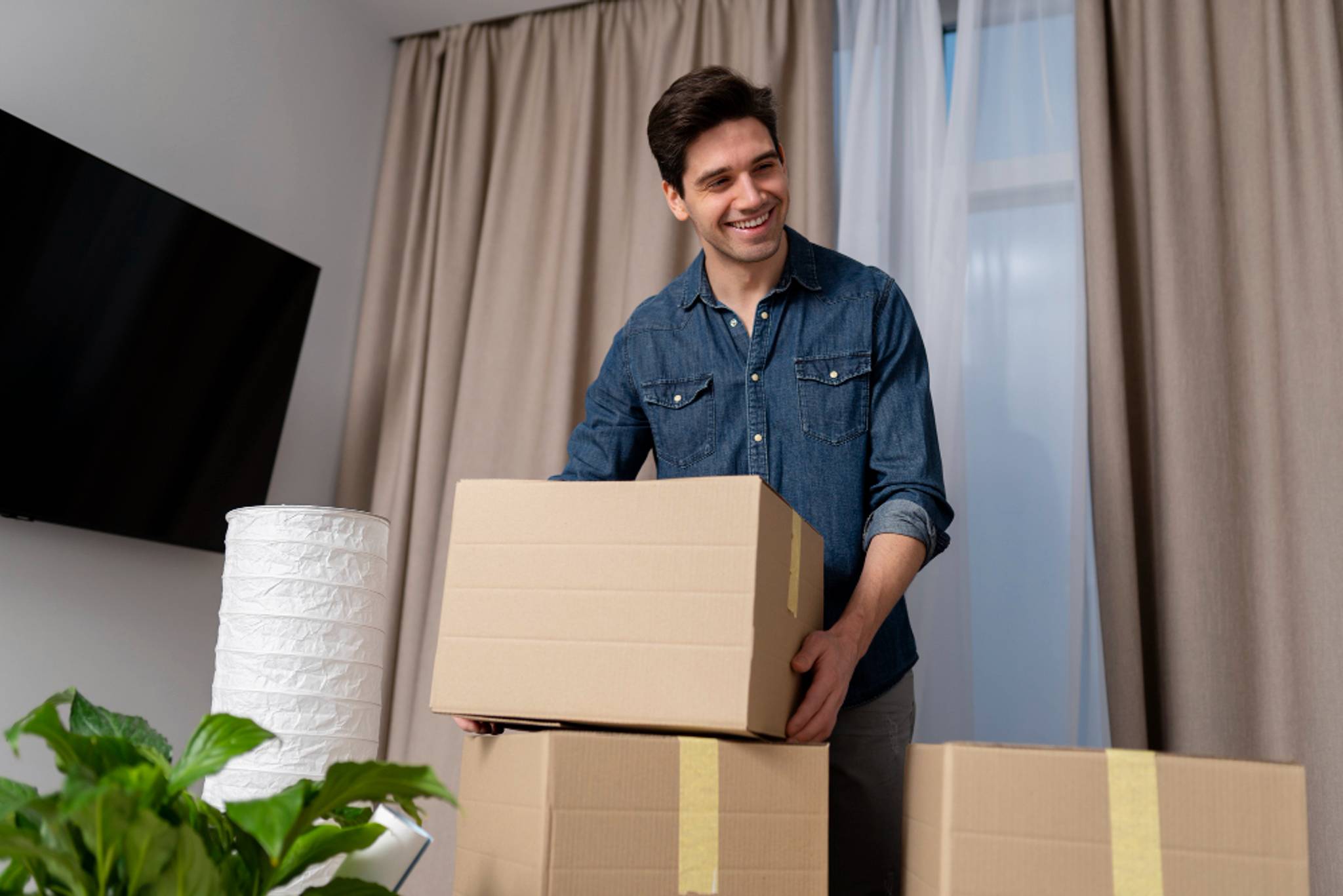 A person smiles at home, placing a box on top of another one, ready for storage