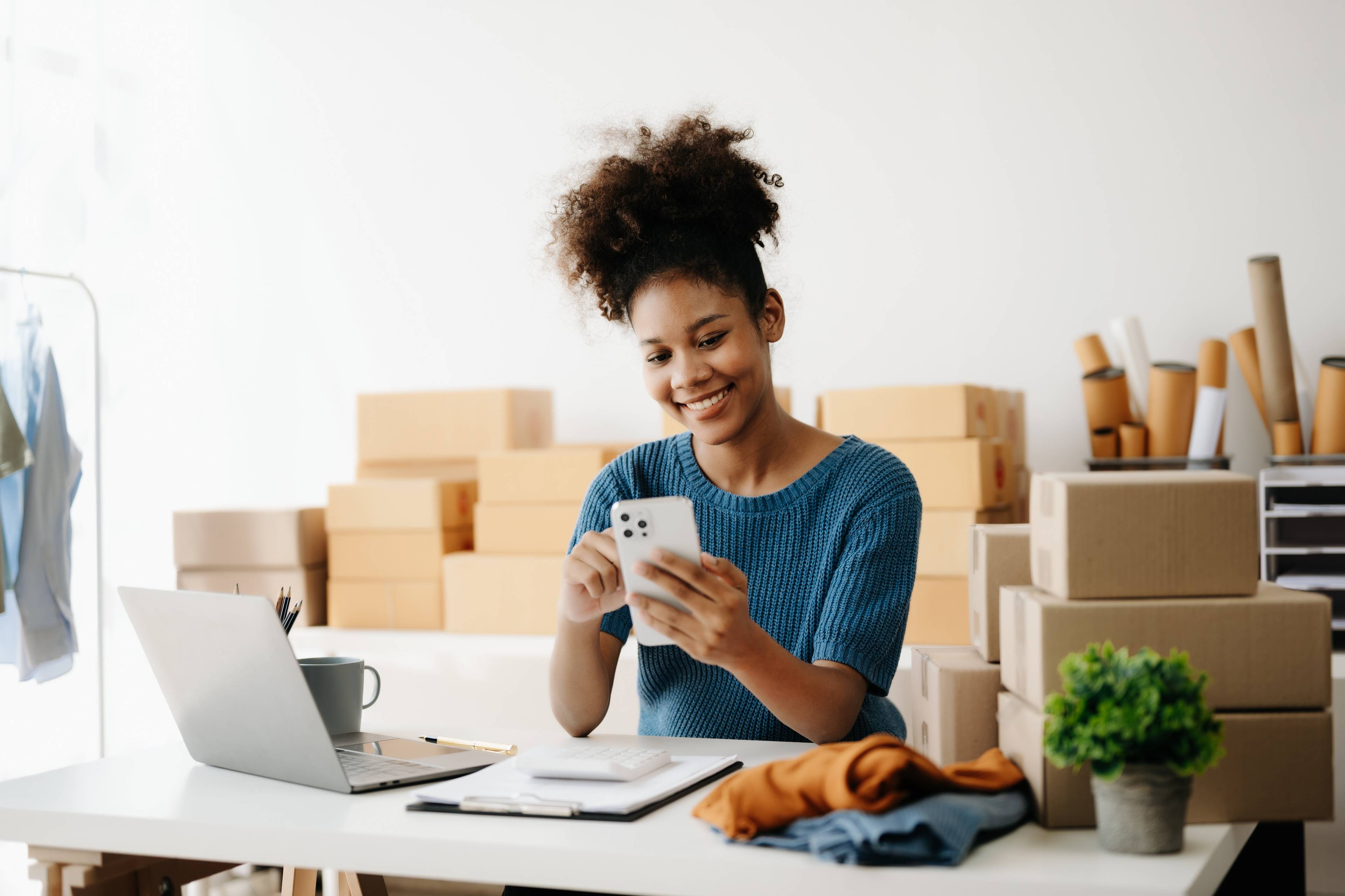 Woman smiling on phone with laptop and boxes in background