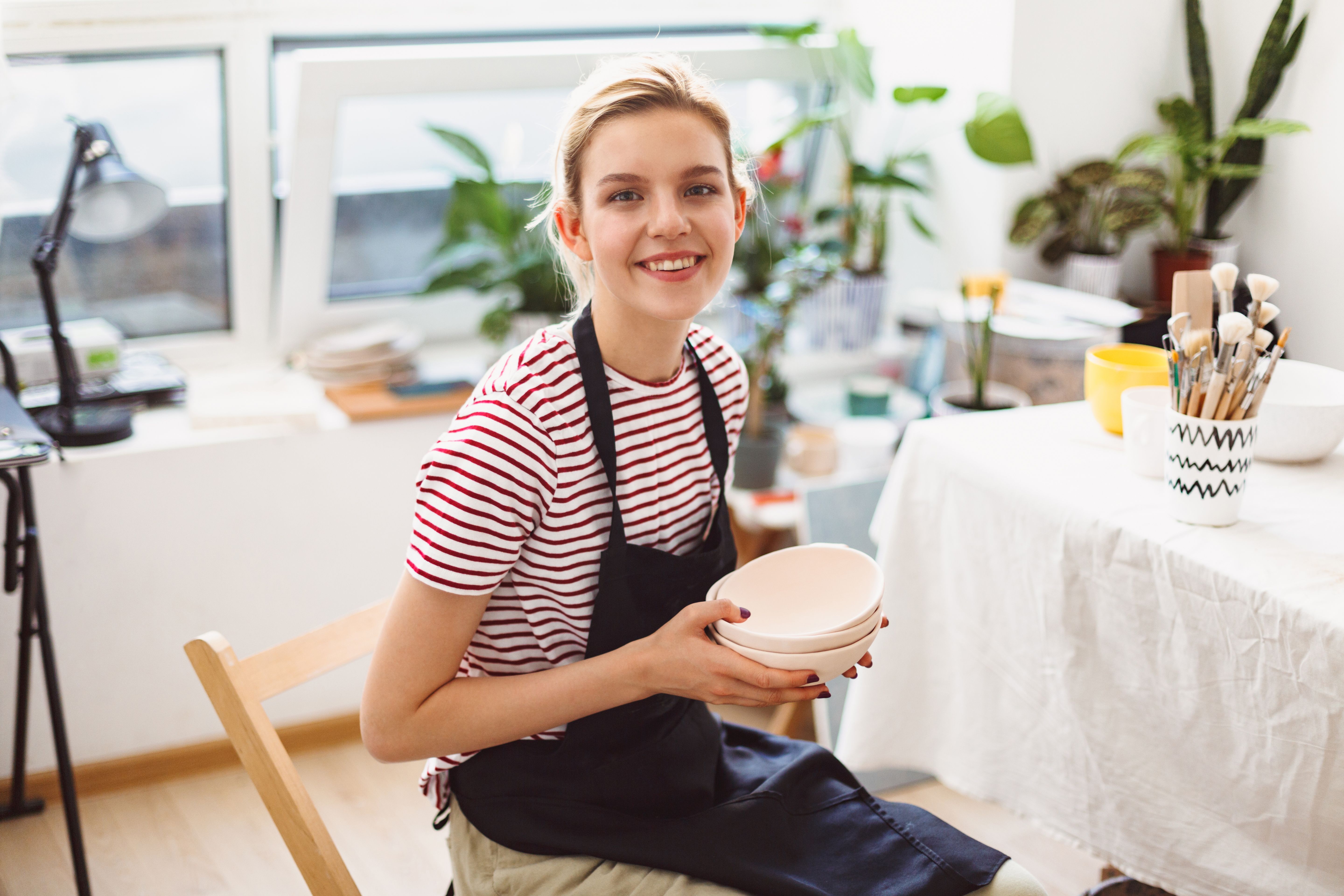 woman smiling wearing apron in bright shop holding bowl