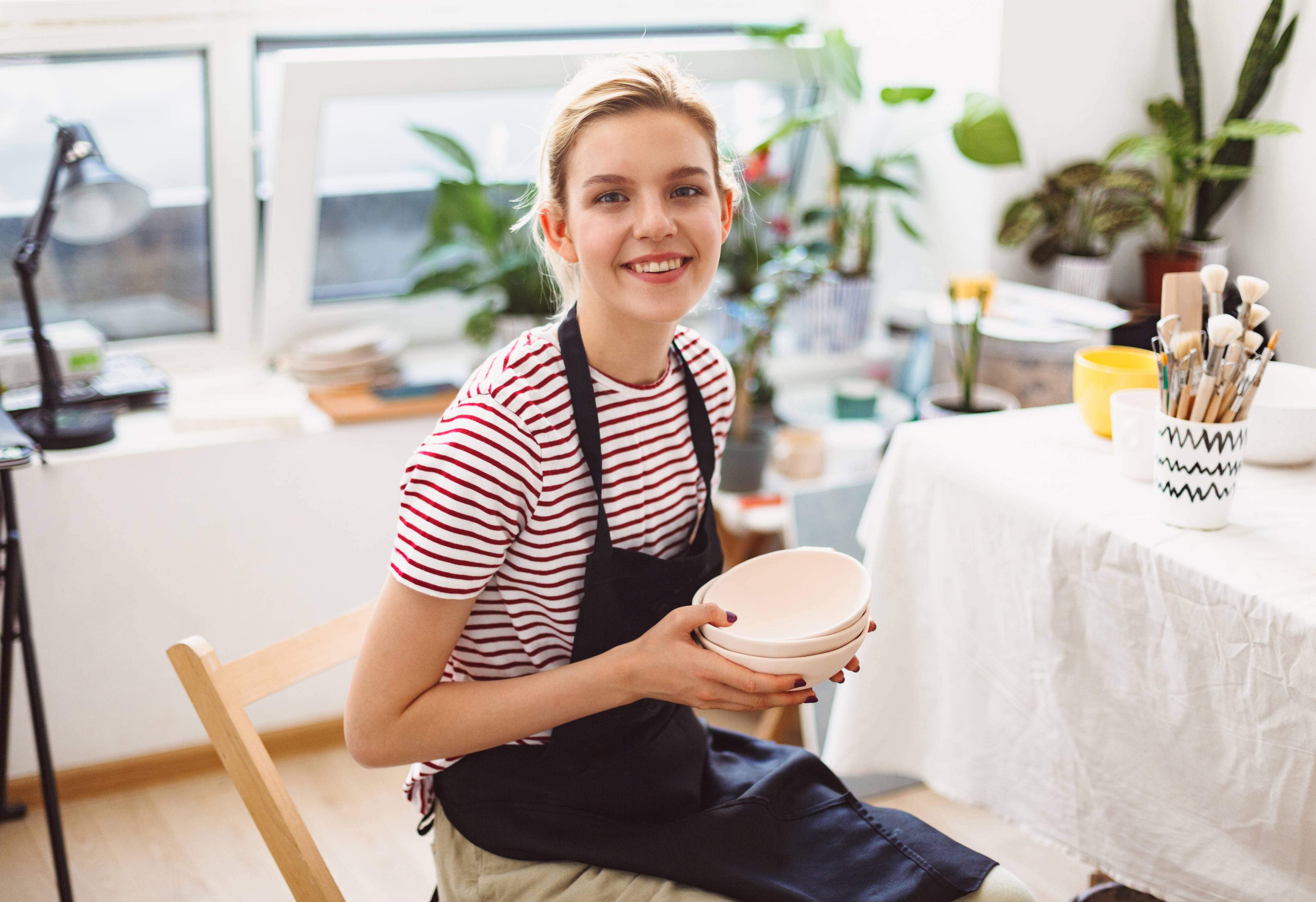 woman smiling wearing apron in bright shop holding bowl