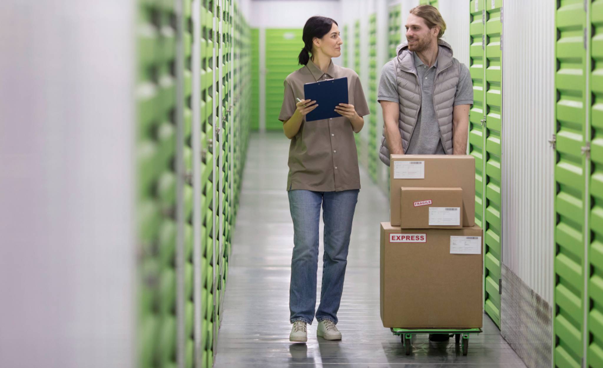 A man moves boxes towards a storage unit while speaking to a woman.
